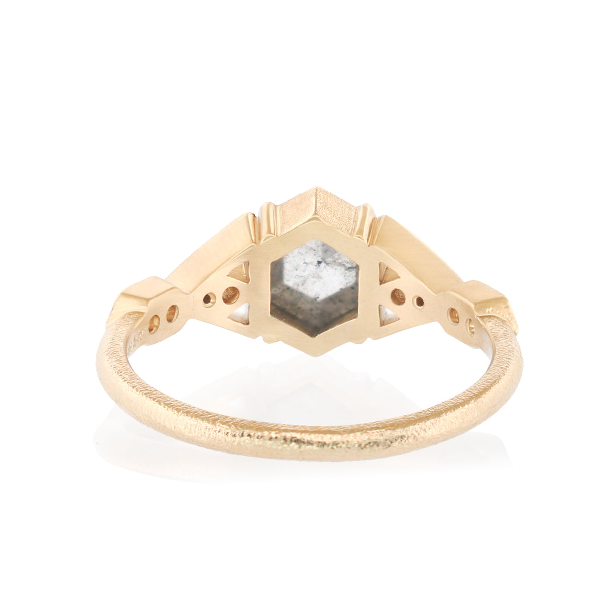 A gold ring with a textured band and a central geometric setting holding a faceted gray gemstone, shown on a clean white background.
