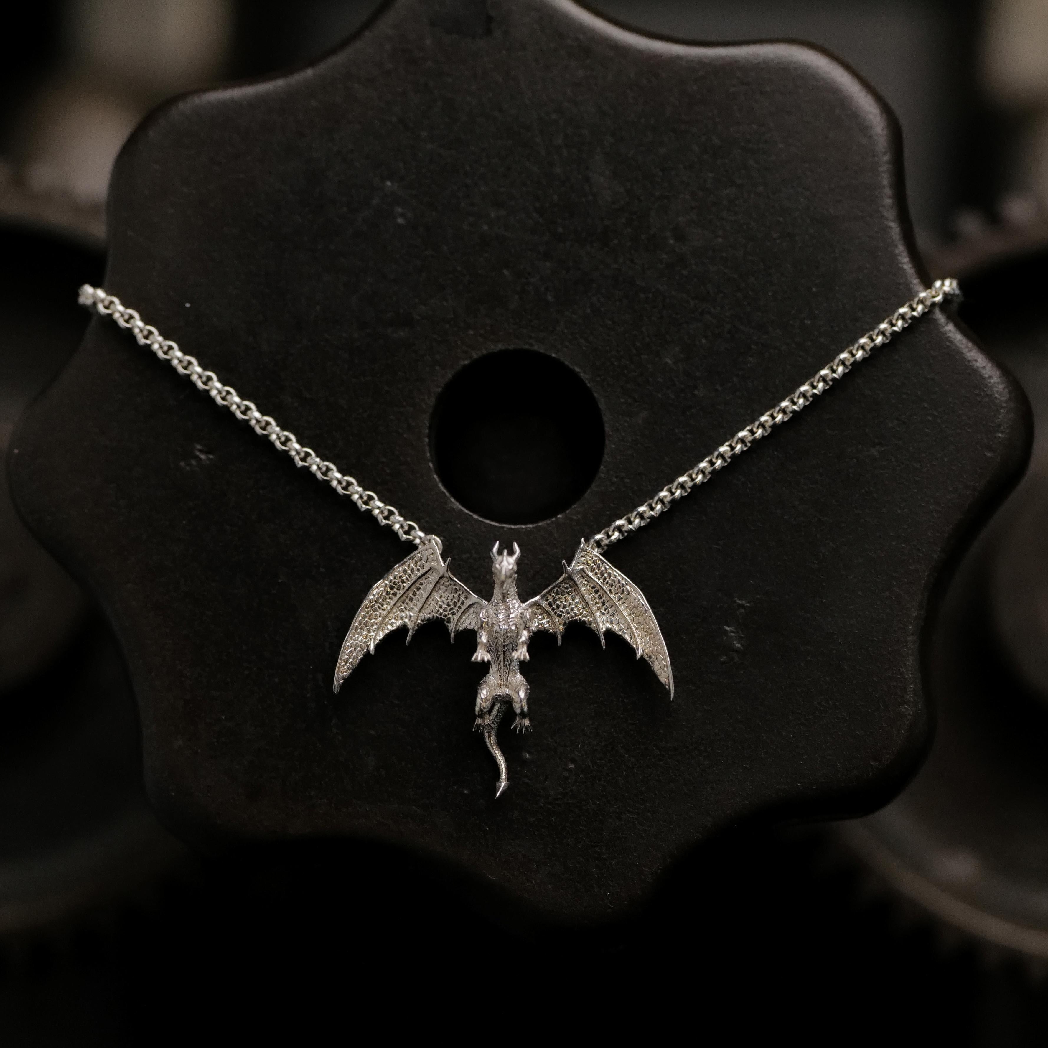 Fiat Lux’s Medieval Dragon Necklace (S) is shown on a dark, gear-shaped background.