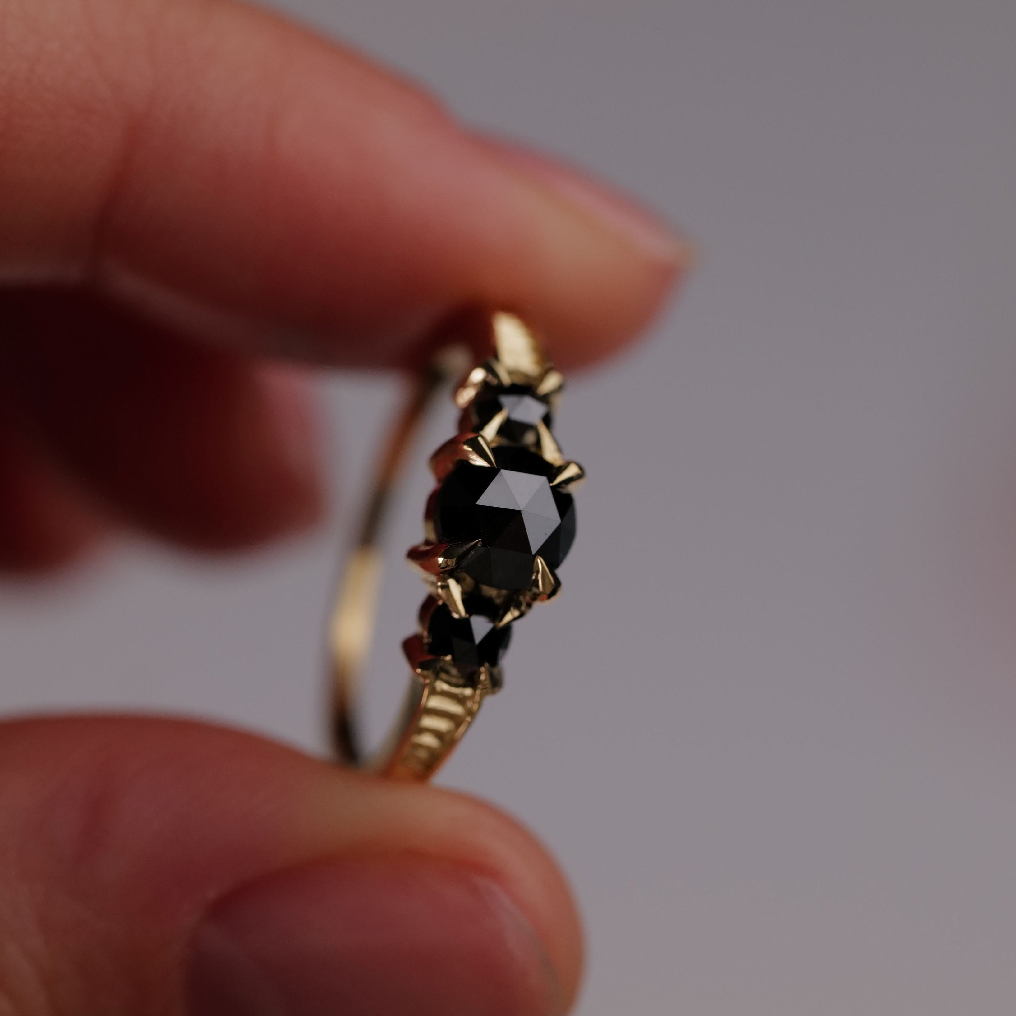 A hand holds Fiat Luxs Classic 3 Stone Temple Ring, set in 18K gold with black diamond center and side stones.