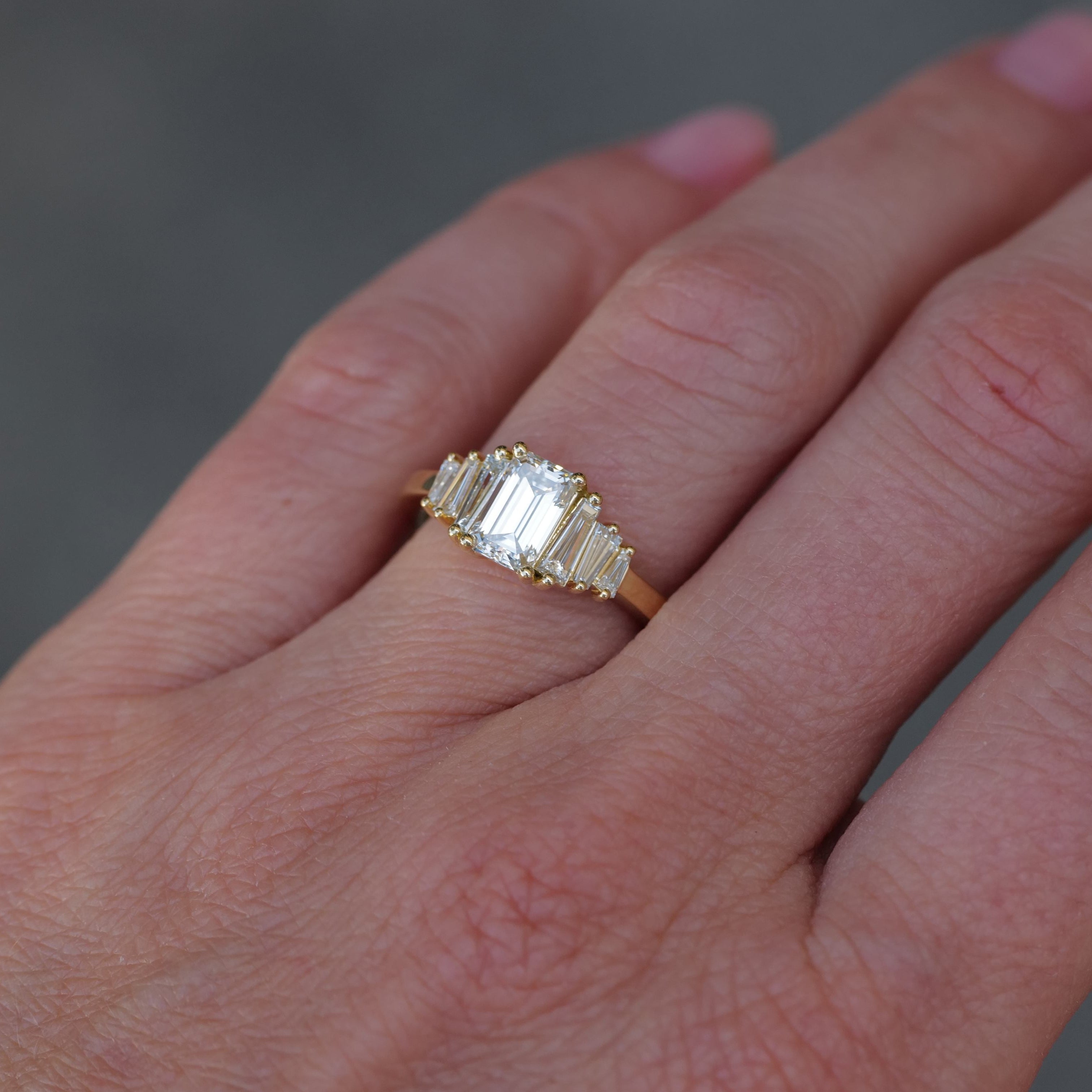 Fiat Lux Classic Calypso 18K gold ring with 1.02ct emerald cut diamond and baguette sides on a hand.