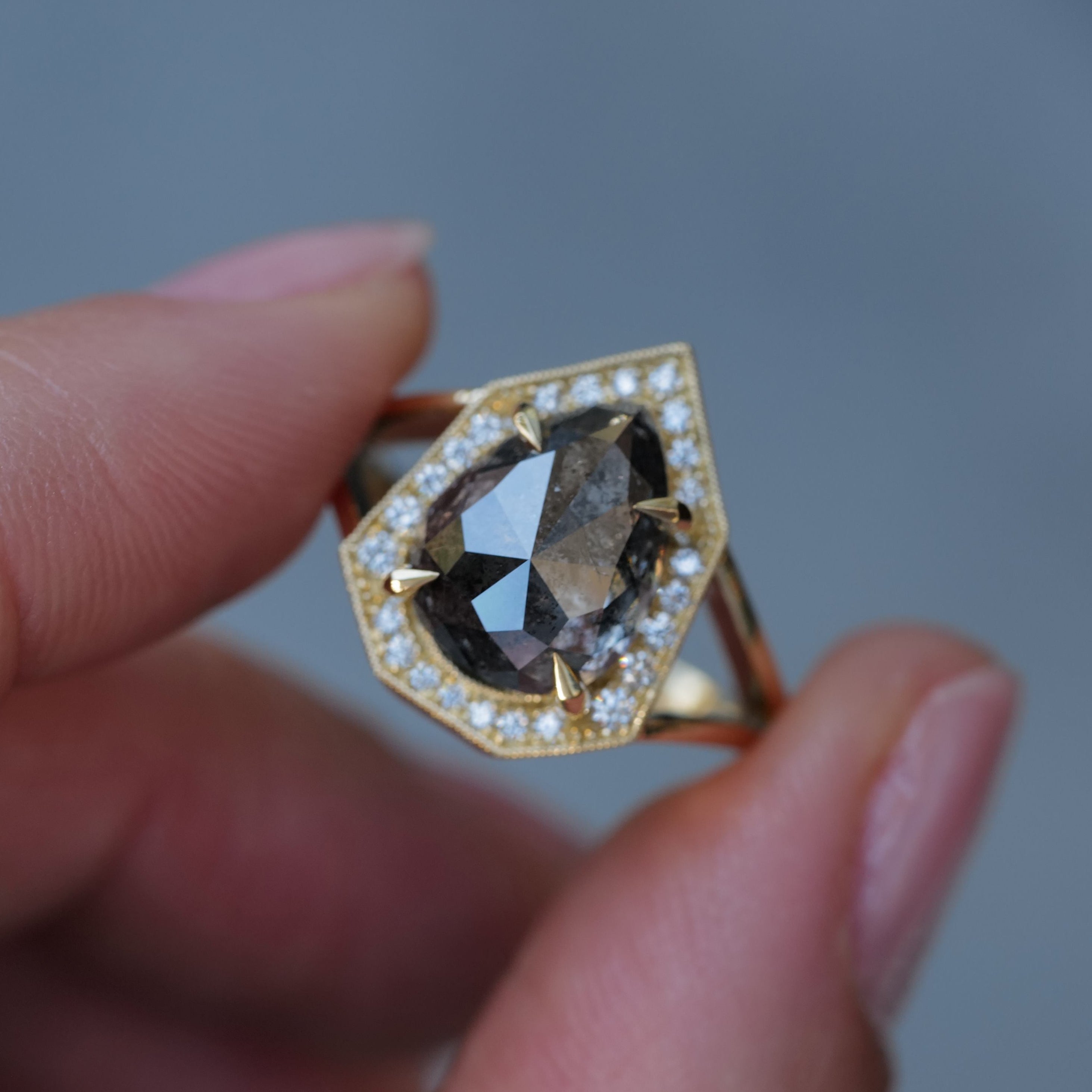 A hand holds Fiat Luxs Grande Phoebe ring (4.88ct salt & pepper diamond, white diamonds) on a gray background.