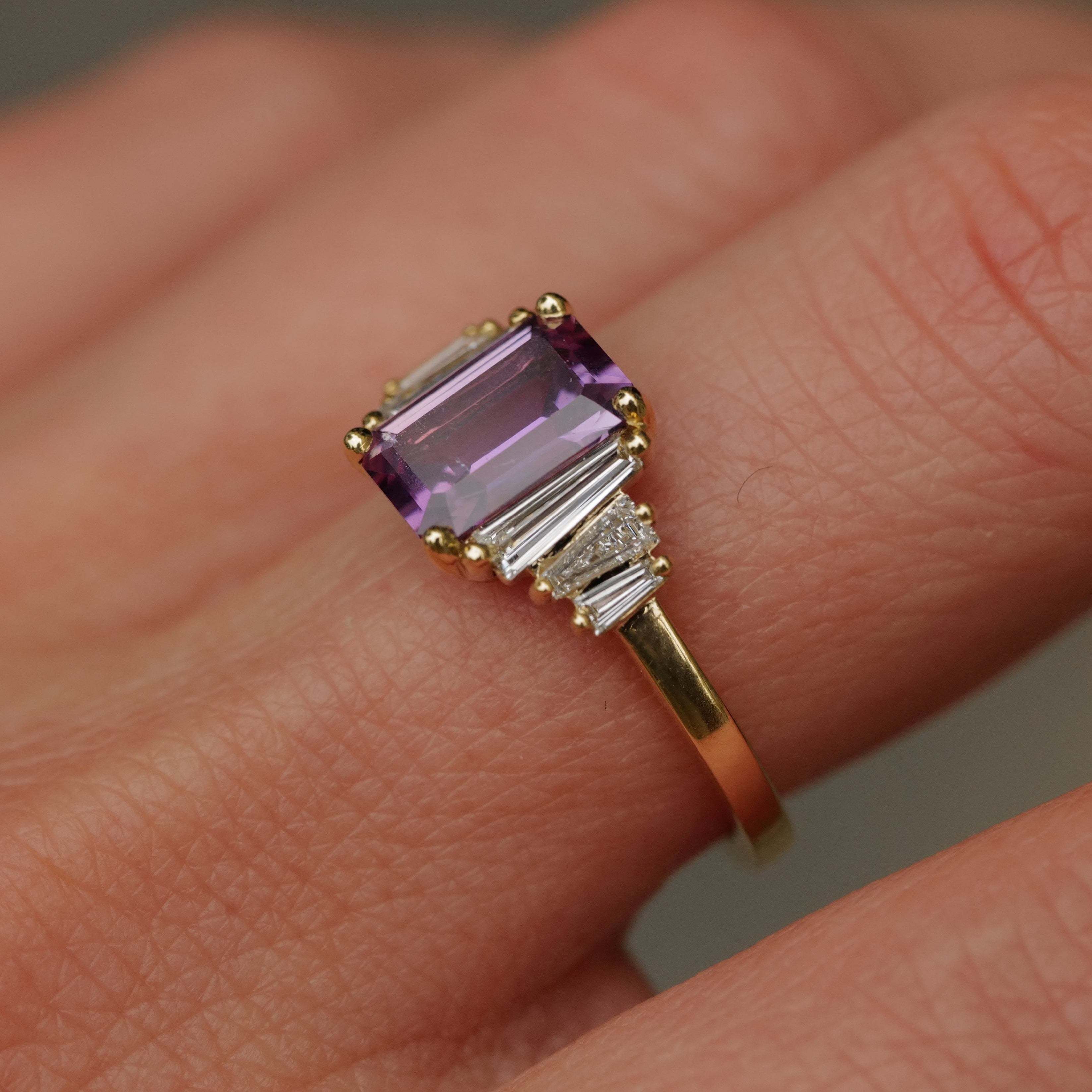 A Fiat Lux Grande Calypso ring with a 1.94ct mulberry pink sapphire and diamond baguettes on a persons finger.