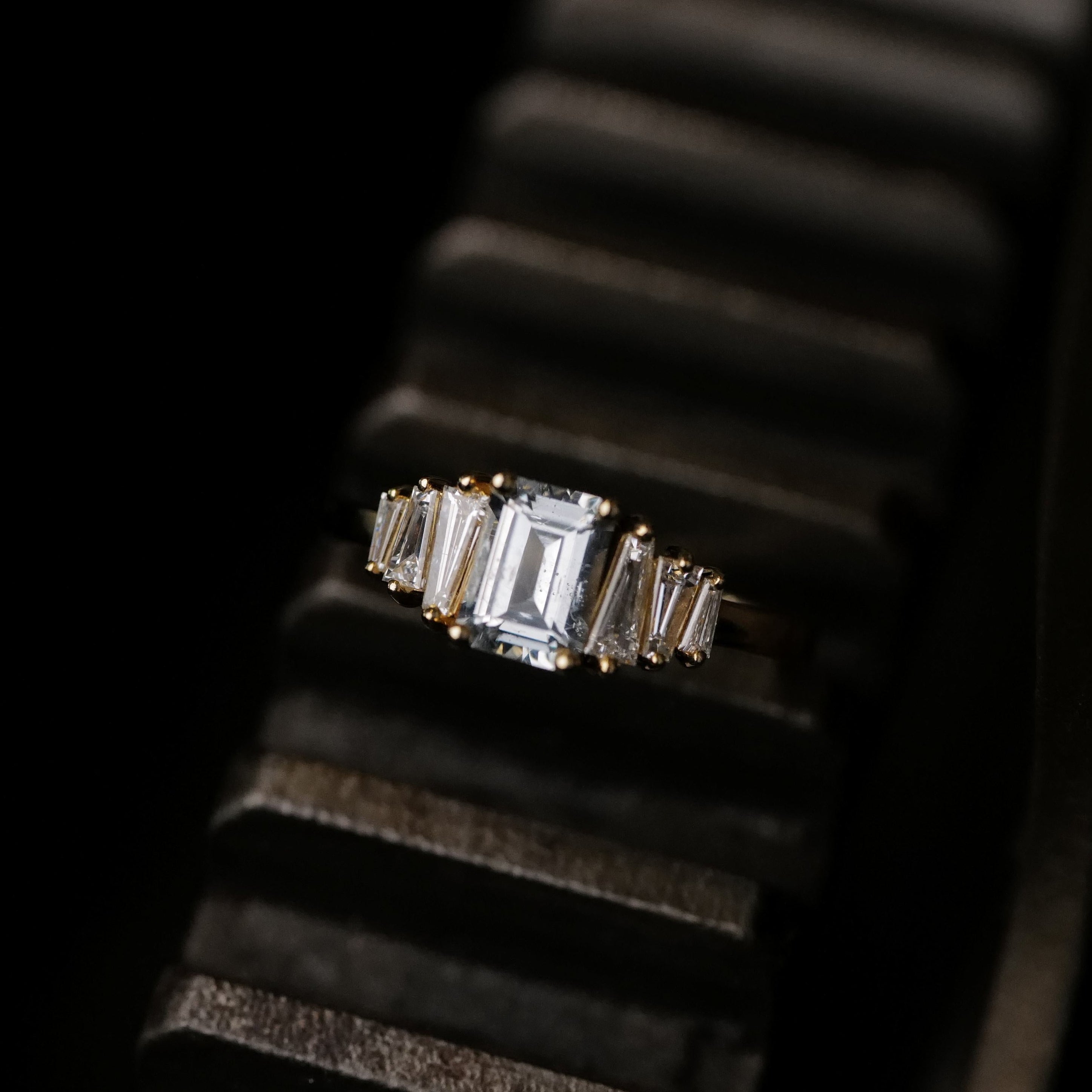 Fiat Lux Petite Calypso ring with a 1.16ct ice blue sapphire, displayed on a black ridged surface.