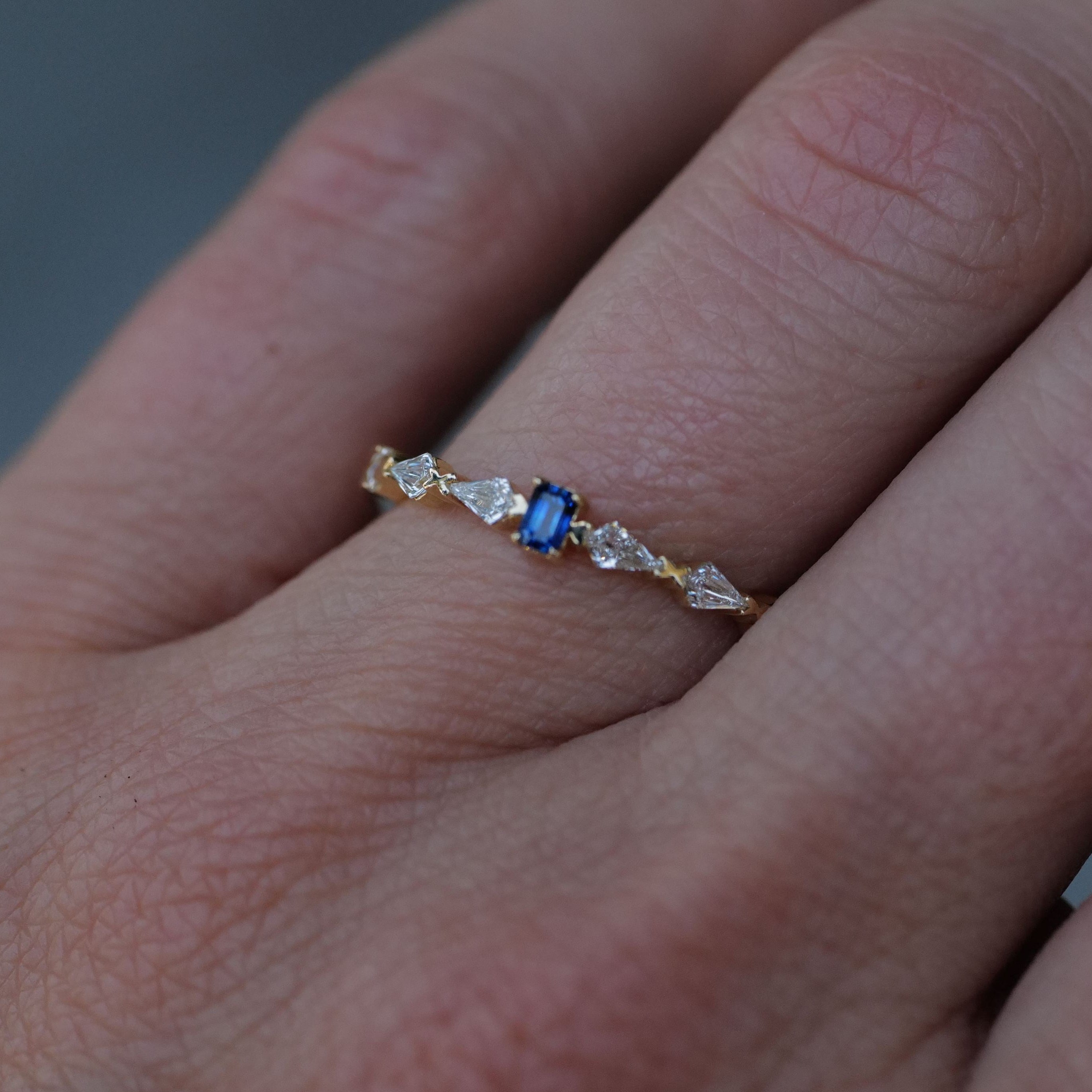 The Fiat Lux Petite Astra Ring, in 14K gold with a blue gemstone and kite diamonds, graces a finger.