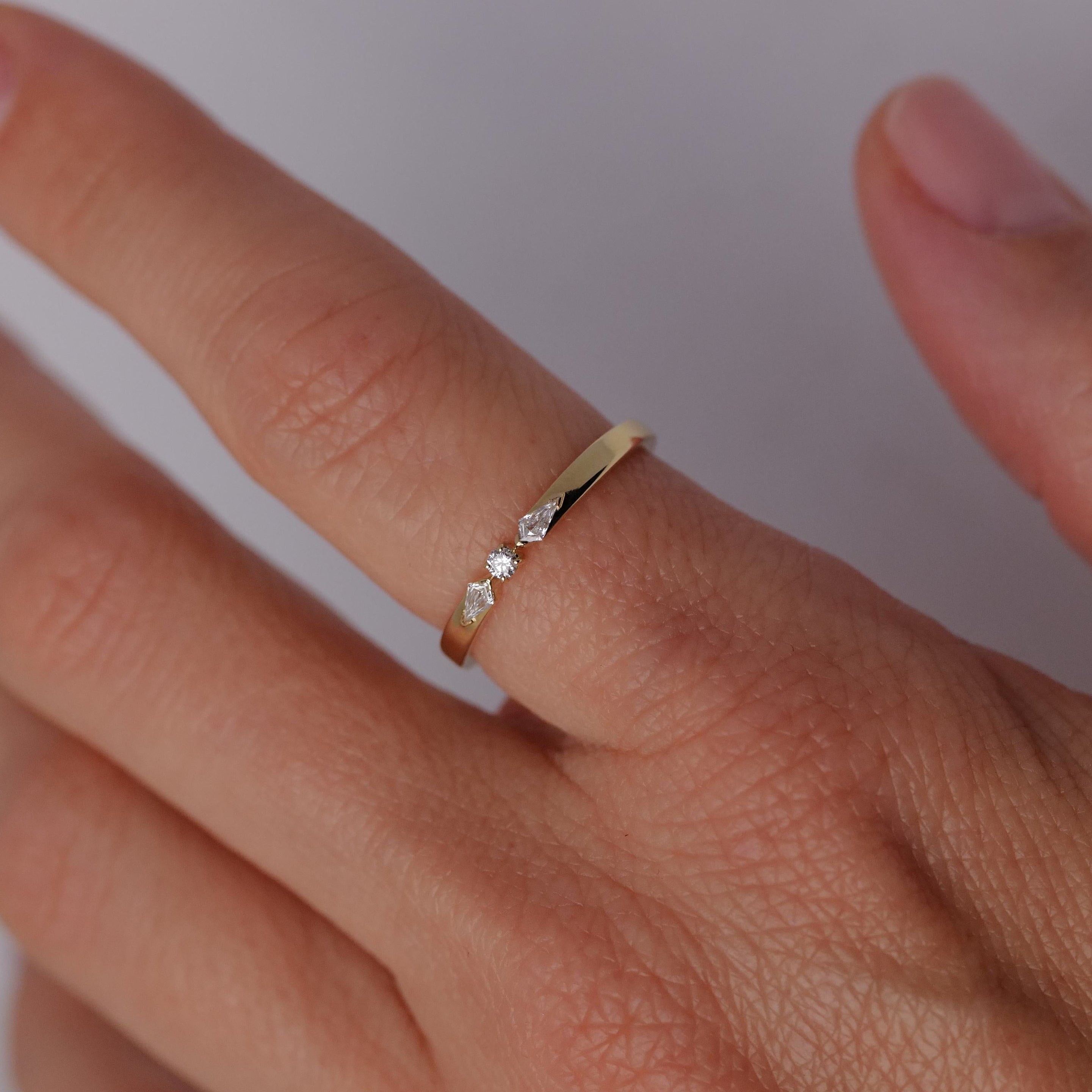 The Fiat Lux Petite Nova Ring is a 14K gold ring with three small diamonds, shown on a finger against a light background.