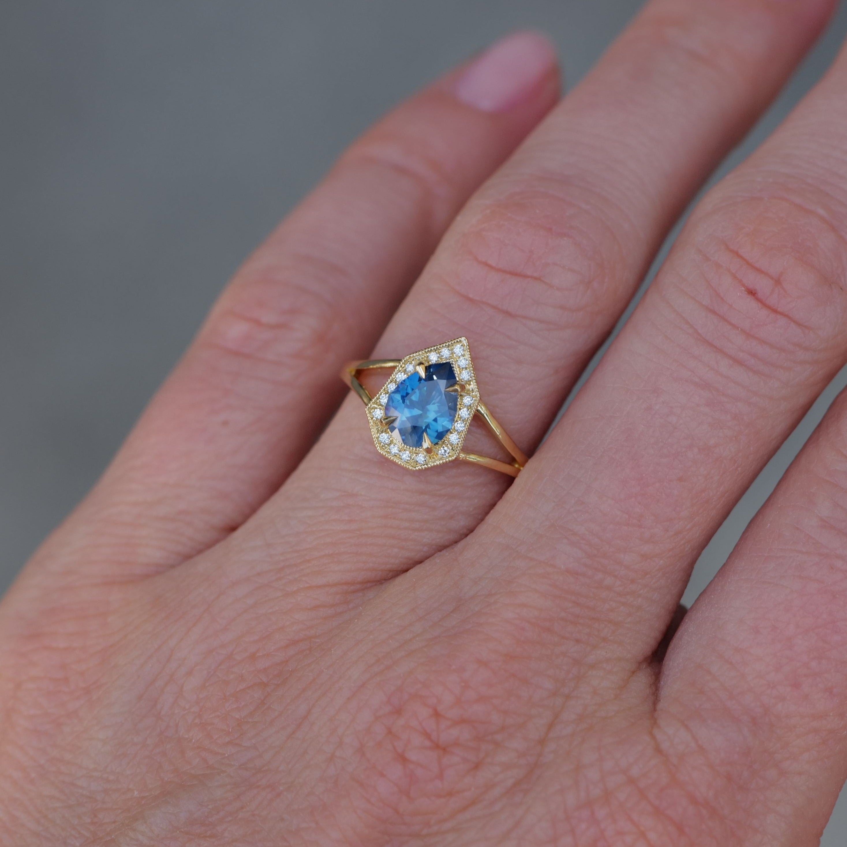 A hand wearing Fiat Luxs Petite Phoebe ring with a 1.15ct denim blue Montana sapphire and diamond halo.