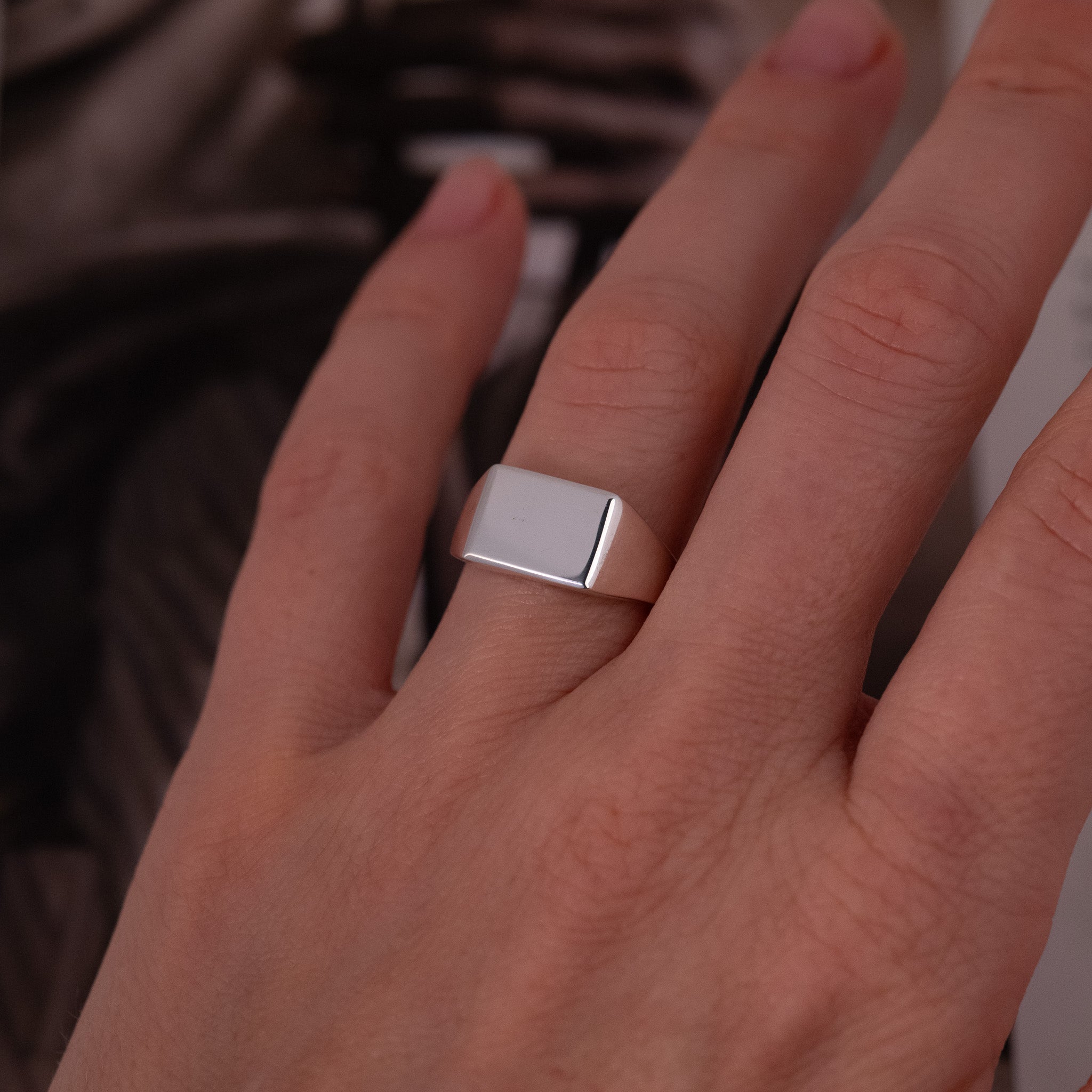 A hand wears the Classic Rectangle Signet Ring - Plain (S) by Fiat Lux on the middle finger, background blurred.