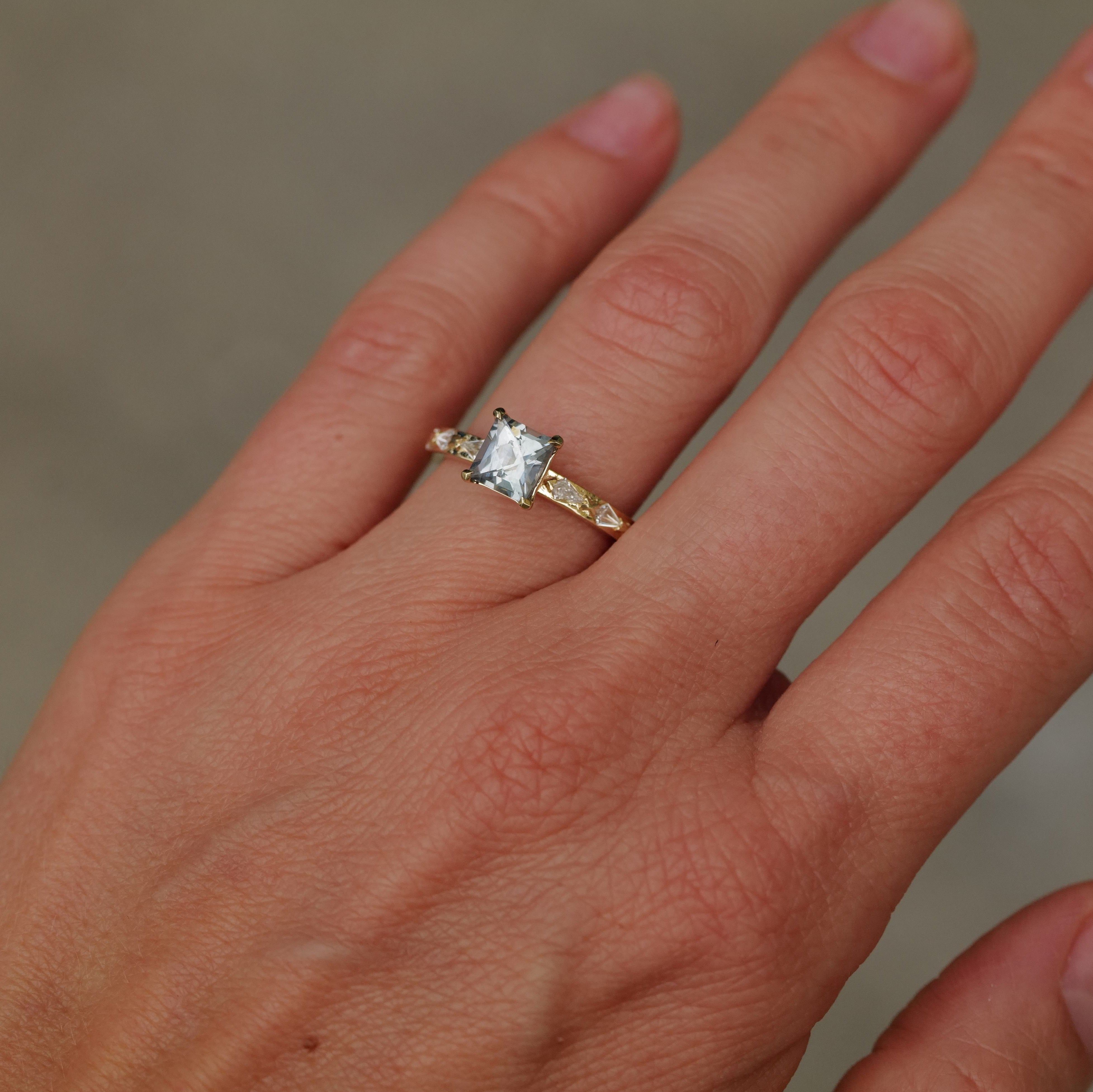 A hand wears the Fiat Lux Classic Theia Ring—14K gold with a 1.41ct square-cut aqua sapphire—on the ring finger.