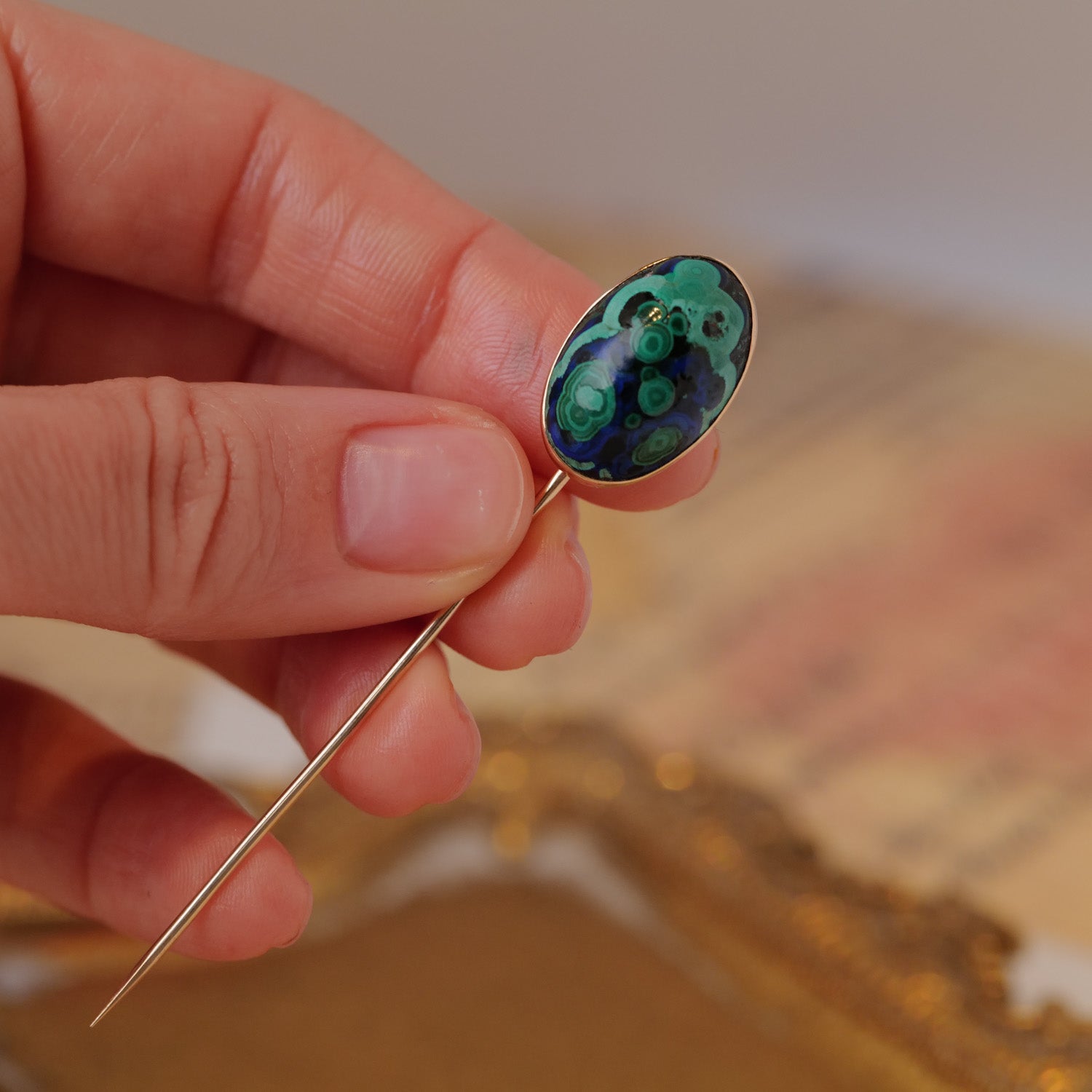 A hand holds a Vintage Antique Azurmalachite Stick Pin with an oval, blue-green patterned decorative head.
