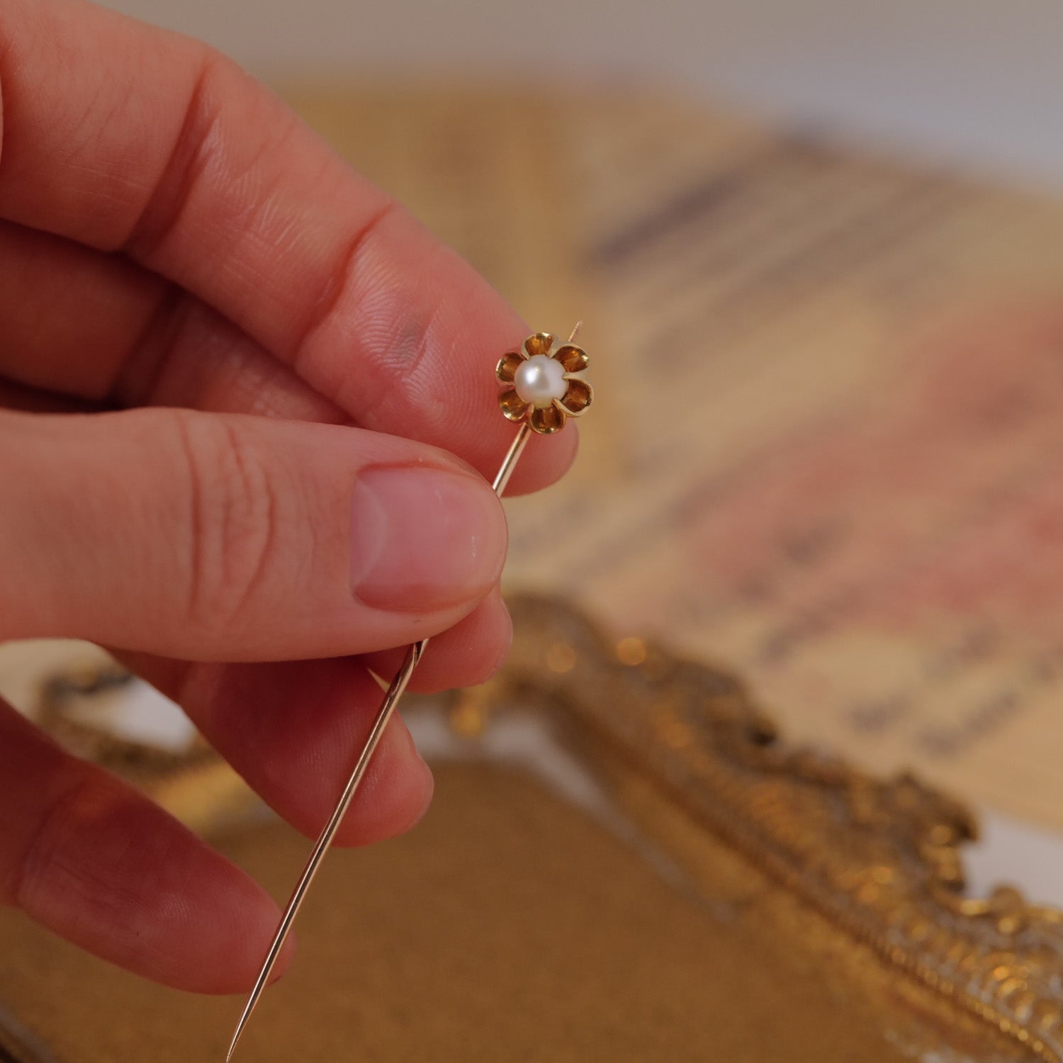 A hand holds the Vintage Antique Pearl Belcher Stick Pin; tray is visible in the background.