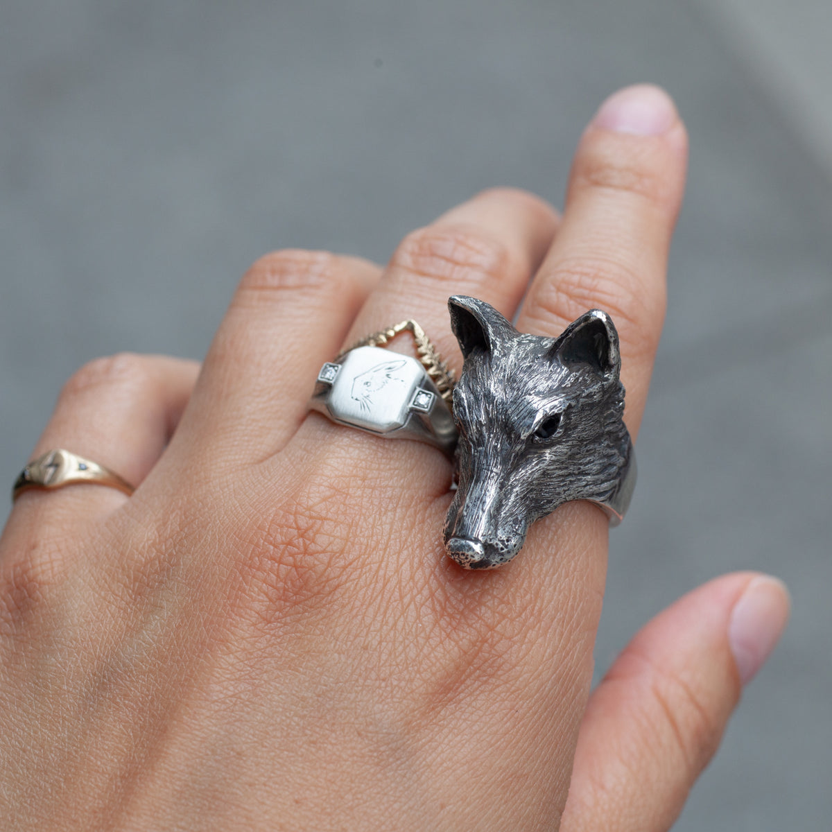 A hand wearing three sterling silver rings, including the Amarok Ring by Allison Bartline, against a gray backdrop.