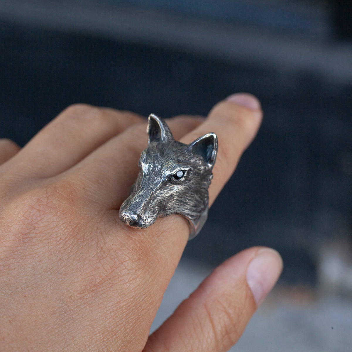 A person wears the Amarok Ring by Allison Bartline, a sterling silver wolf head design, against a dark background.