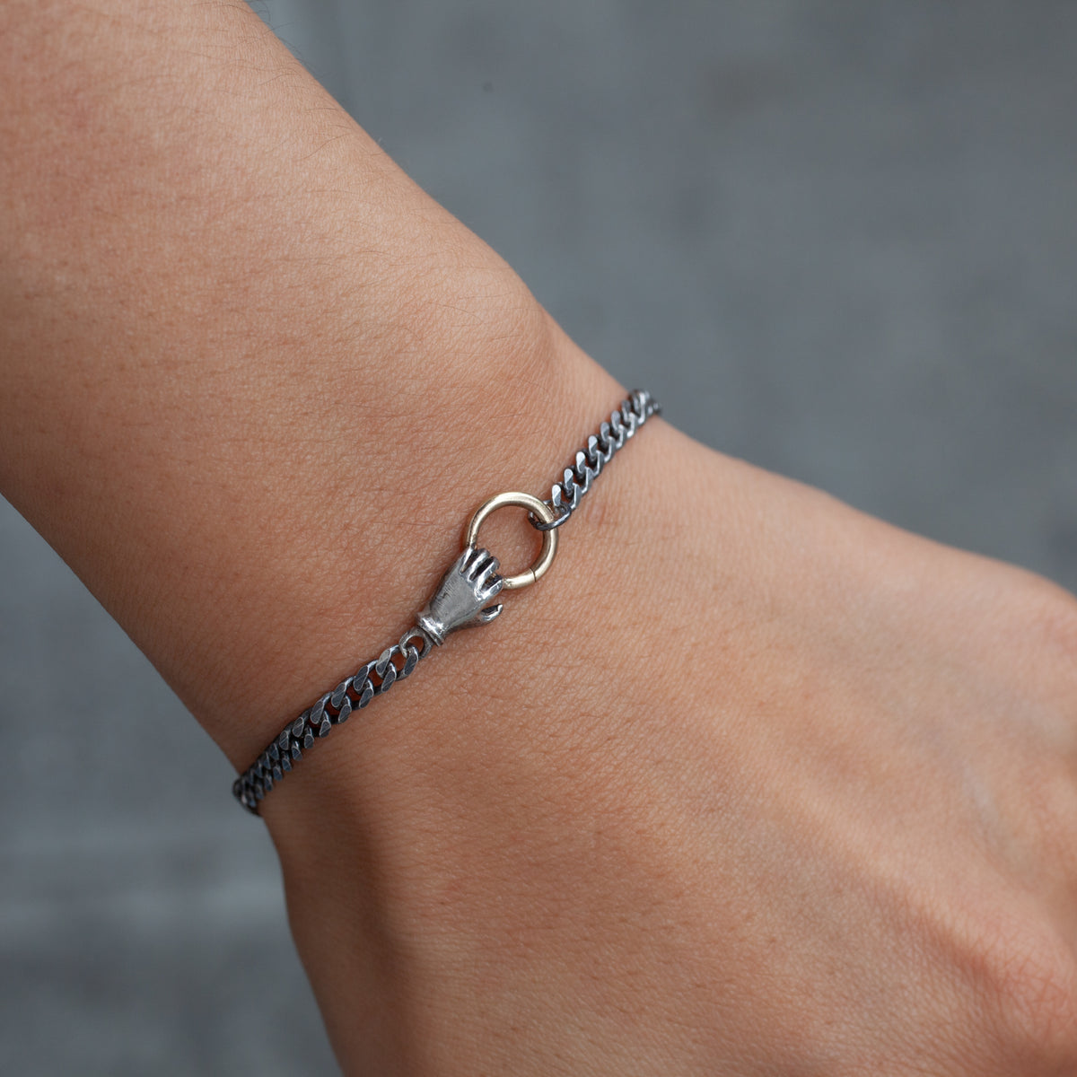 Acanthus’s Fob Grip Bracelet: a sterling silver curb chain with a hand-shaped charm holding a 14K gold ring.
