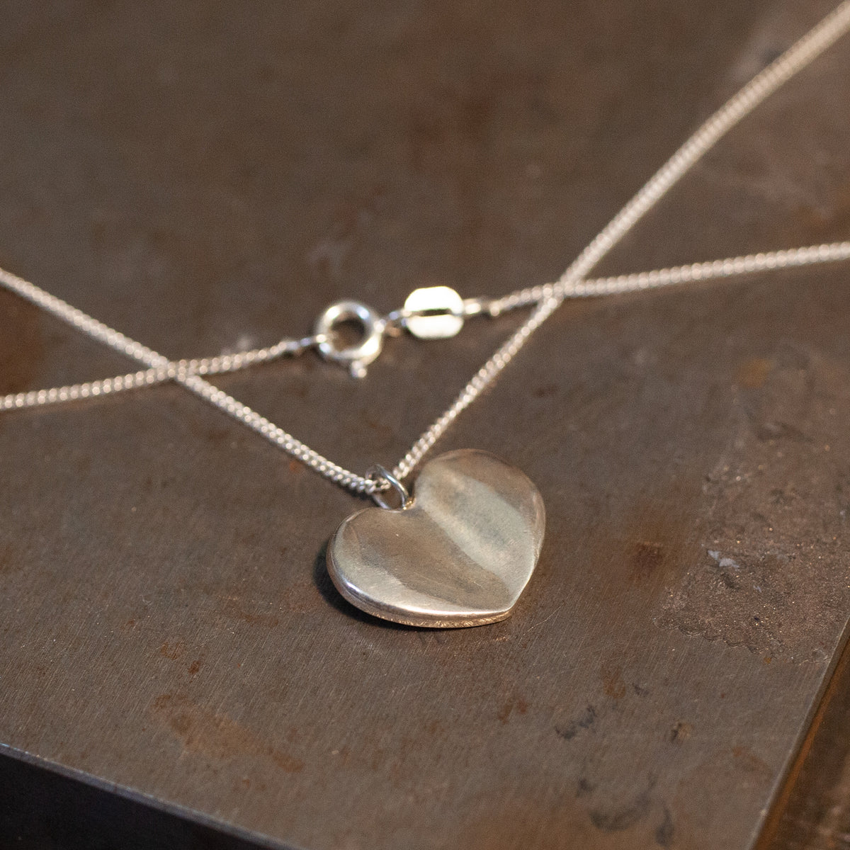 The Grimm Necklace by Ali Munn features a silver heart pendant on sterling chain, inspired by American Traditional style.