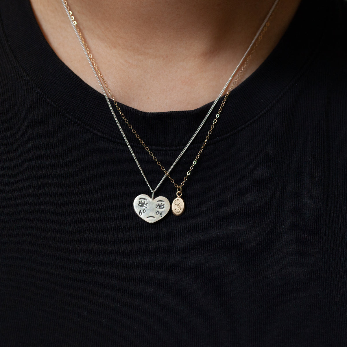 Ali Munn’s Grimm Necklace: a duo of layered chains with an eye-detailed broken heart and a petite oval charm.