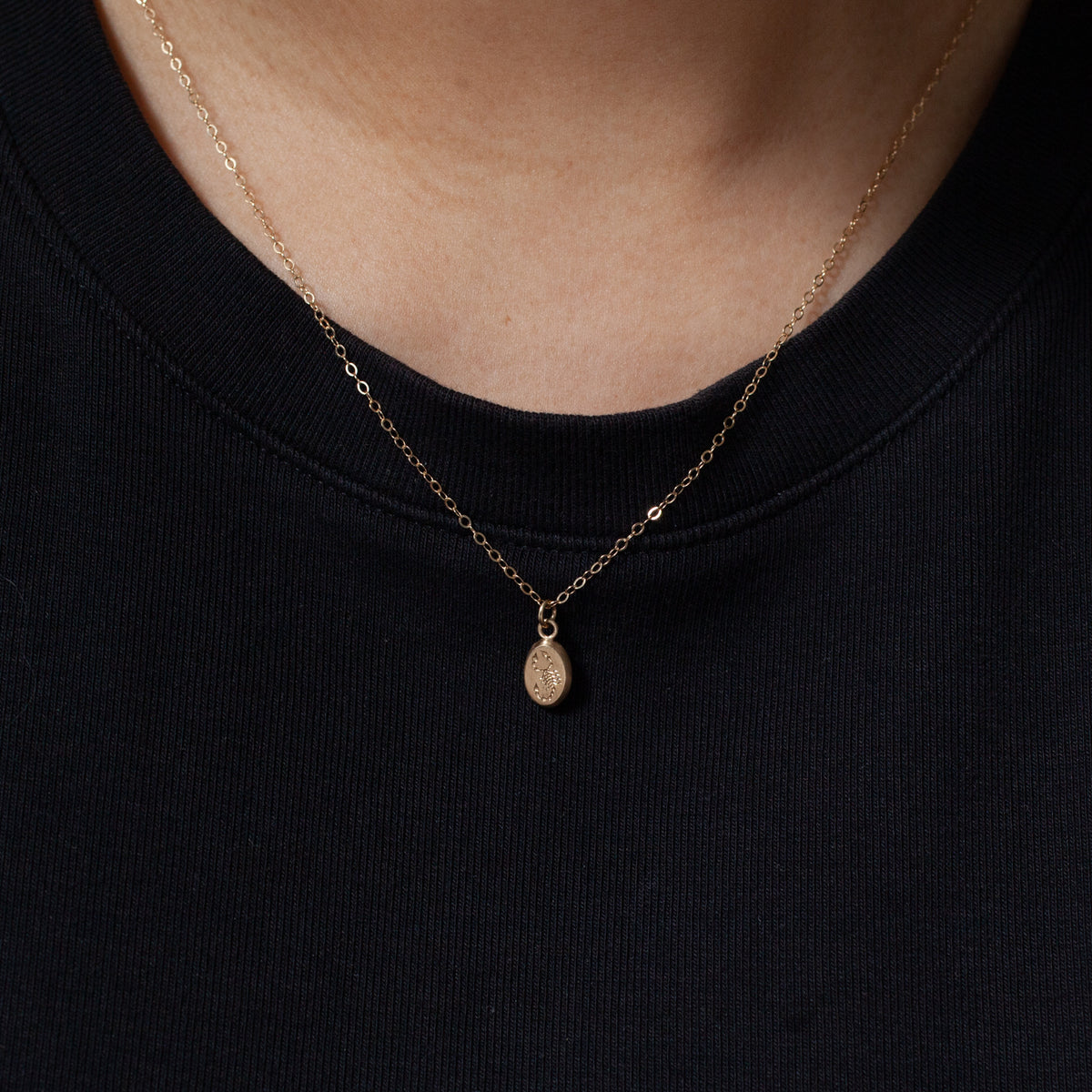 Blue Blue Driver Tiniest Scorpion Necklace in 14K gold, with tiny oval pendant, over a black ribbed shirt.