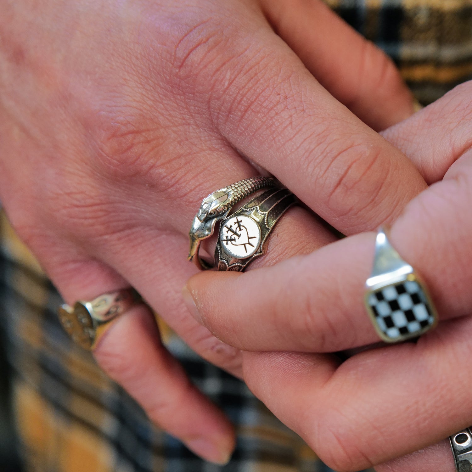 Hand with four Digby & Iona sterling silver rings: Resting Nagini, checkered, engraved, and round designs shown.