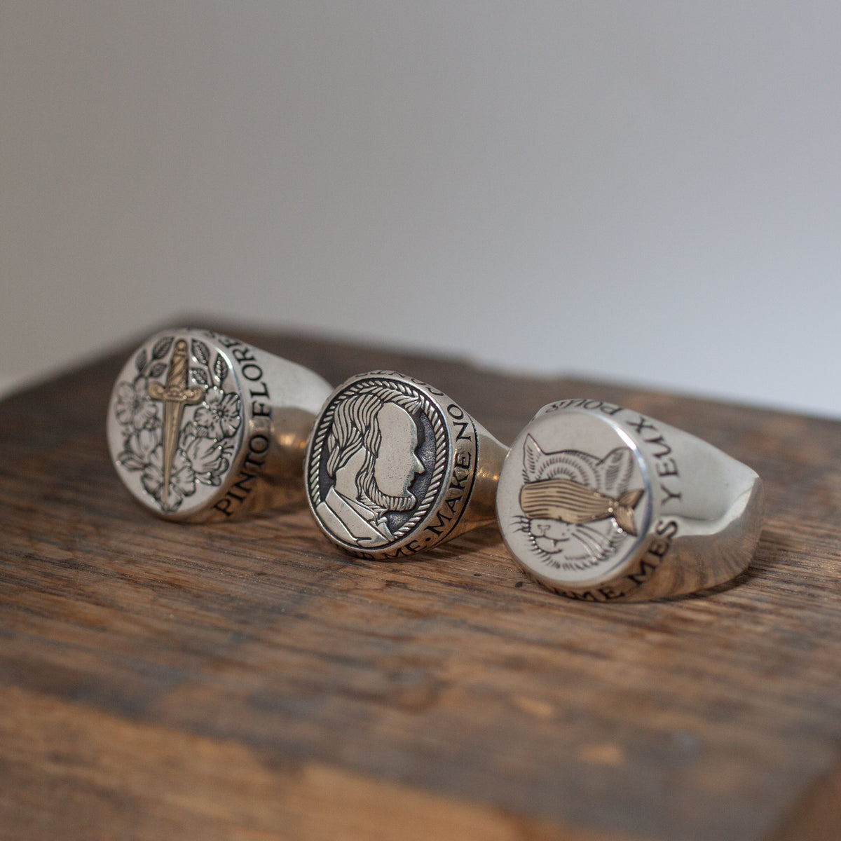 Three sterling silver rings on wood: sword with flowers, Digby & Iona’s Honest Abe Signet Ring, and fox head in a hat.