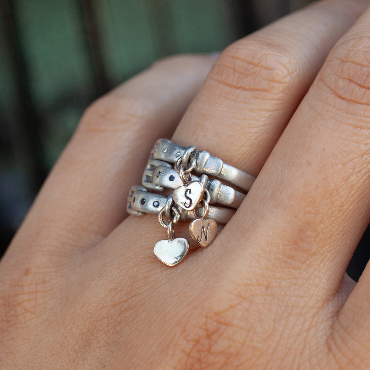 Three antique-inspired Little Love Pet Collar Ring - Black Diamond rings on a finger with two heart-shaped S and N charms.