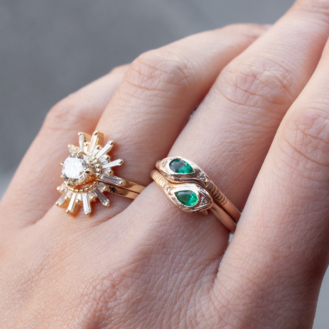 Two gold rings—one sunburst, the other Daisy San Luis’s Victorias Fede Ring with emerald shimmer—adorn her hand.