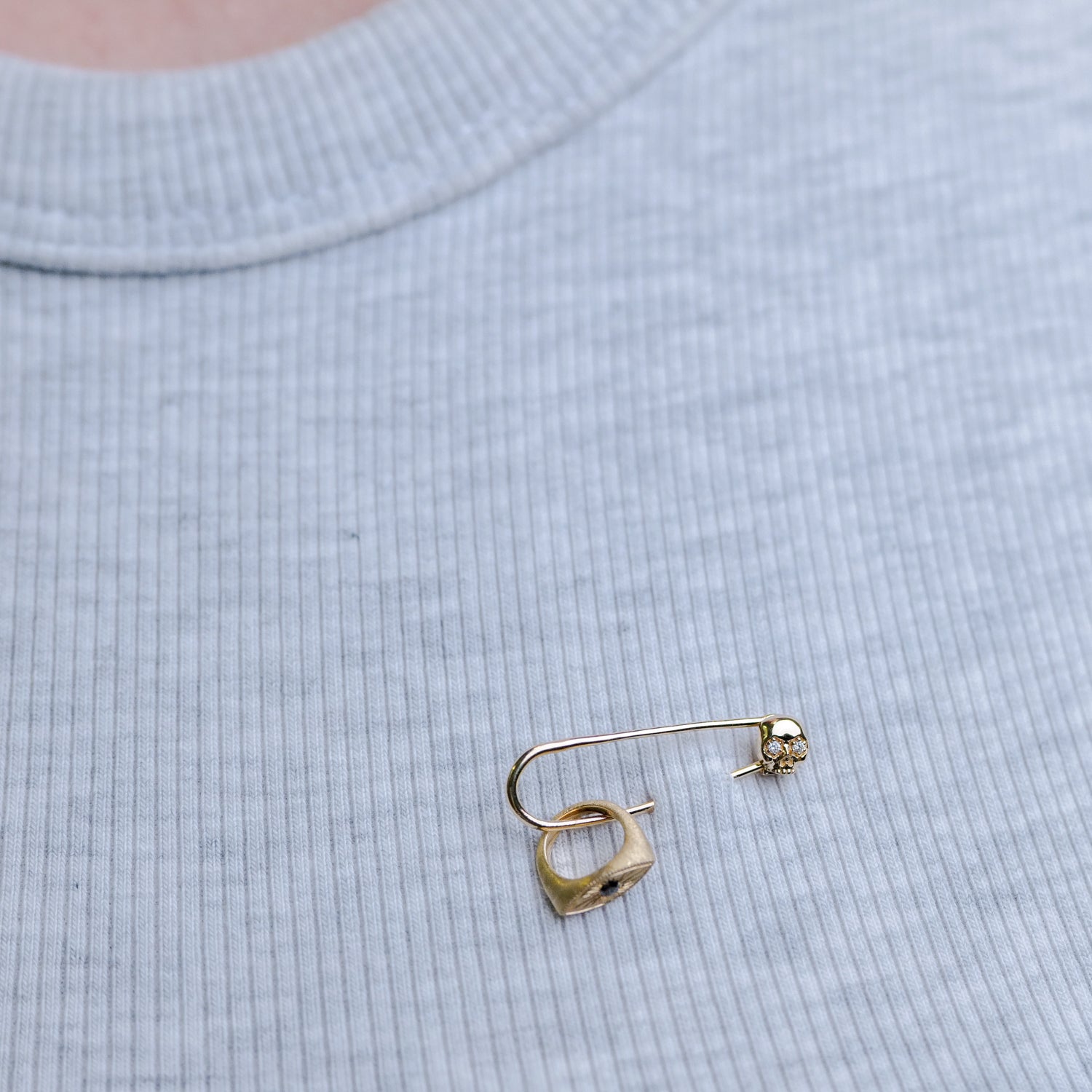 A Fiat Lux Skull Charm Holder is fastened to a light gray ribbed shirt.