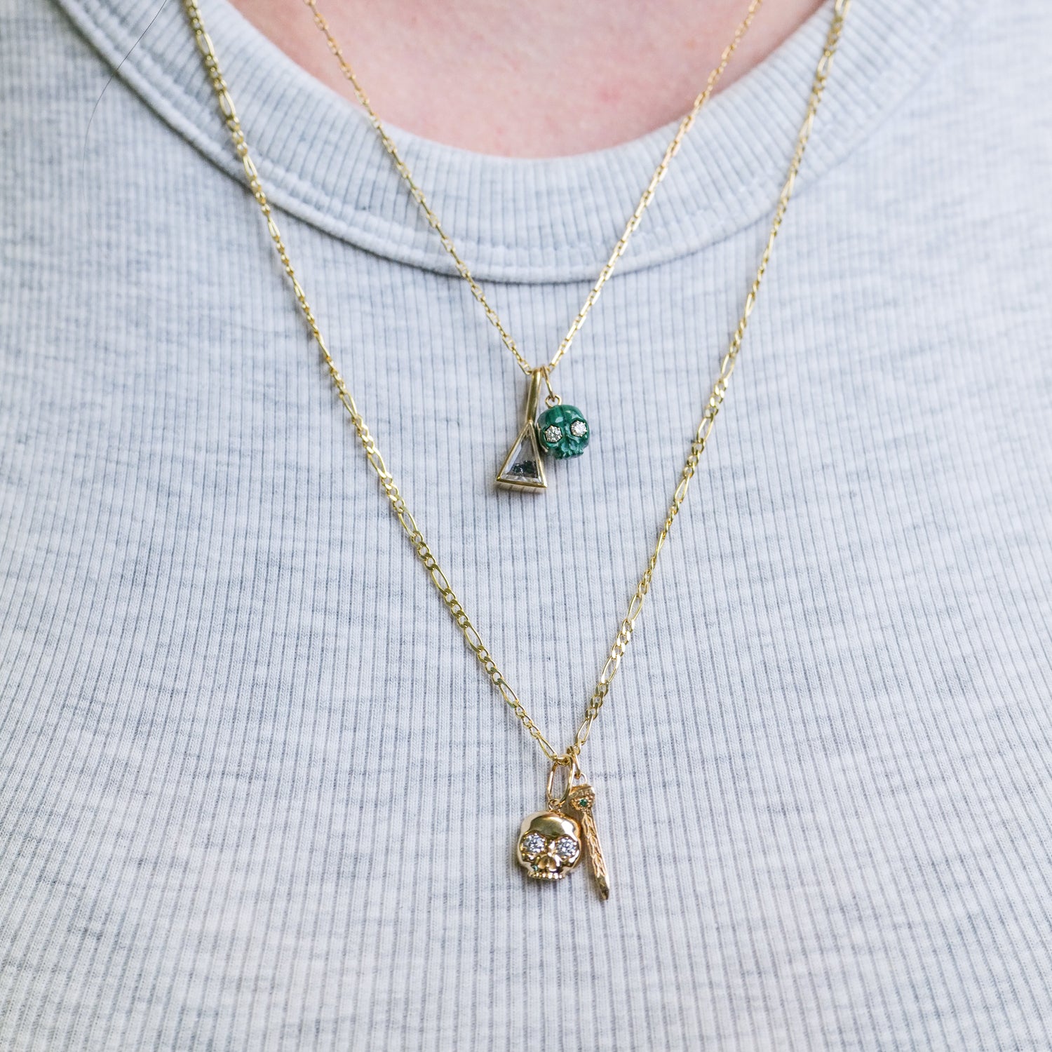 Fiat Luxs The Skull of Bloodstone: two gold necklaces with bloodstone skull and gems, styled on a light gray ribbed shirt.