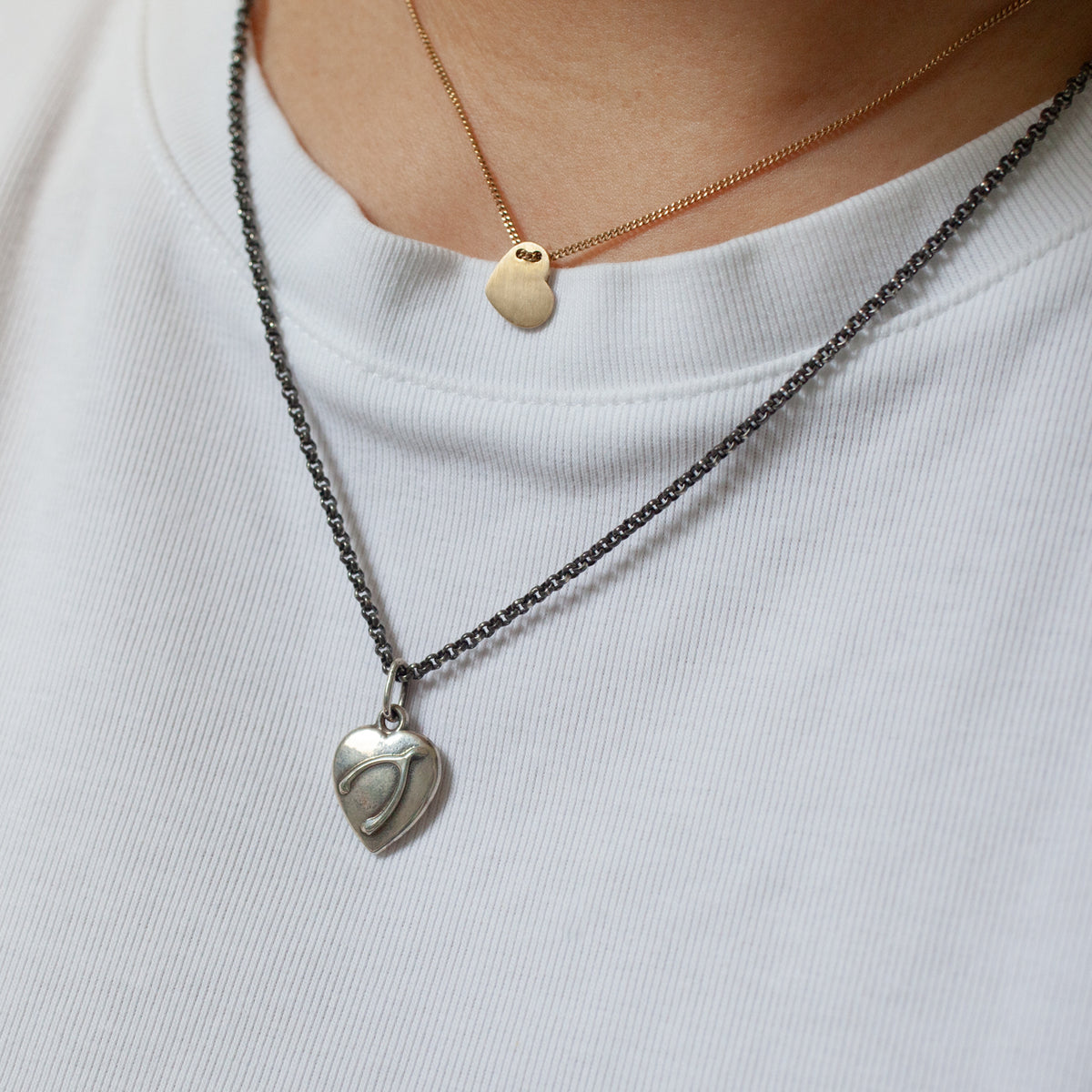 Fiat Lux Wishbone Heart Charm (S) necklaces in gold and silver, styled over a white ribbed shirt.