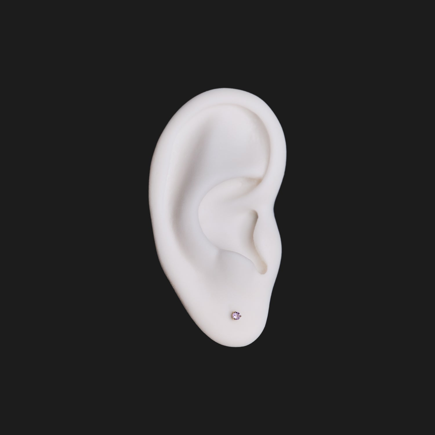 A white model ear with Fiat Lux’s 3 Prong Round - Colored Gems (2mm) earring, set on a black background.