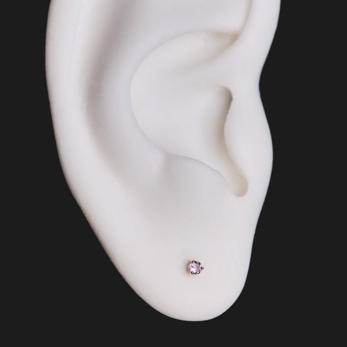 A white model ear with Fiat Lux’s 3 Prong Round - Colored Gems (2mm) earring, set on a black background.