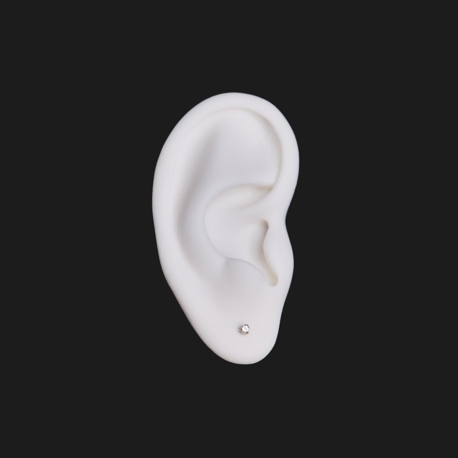 A white ear model wears Fiat Lux’s 3 Prong Round Colored Gem (2mm) stud, shown on a solid black background.