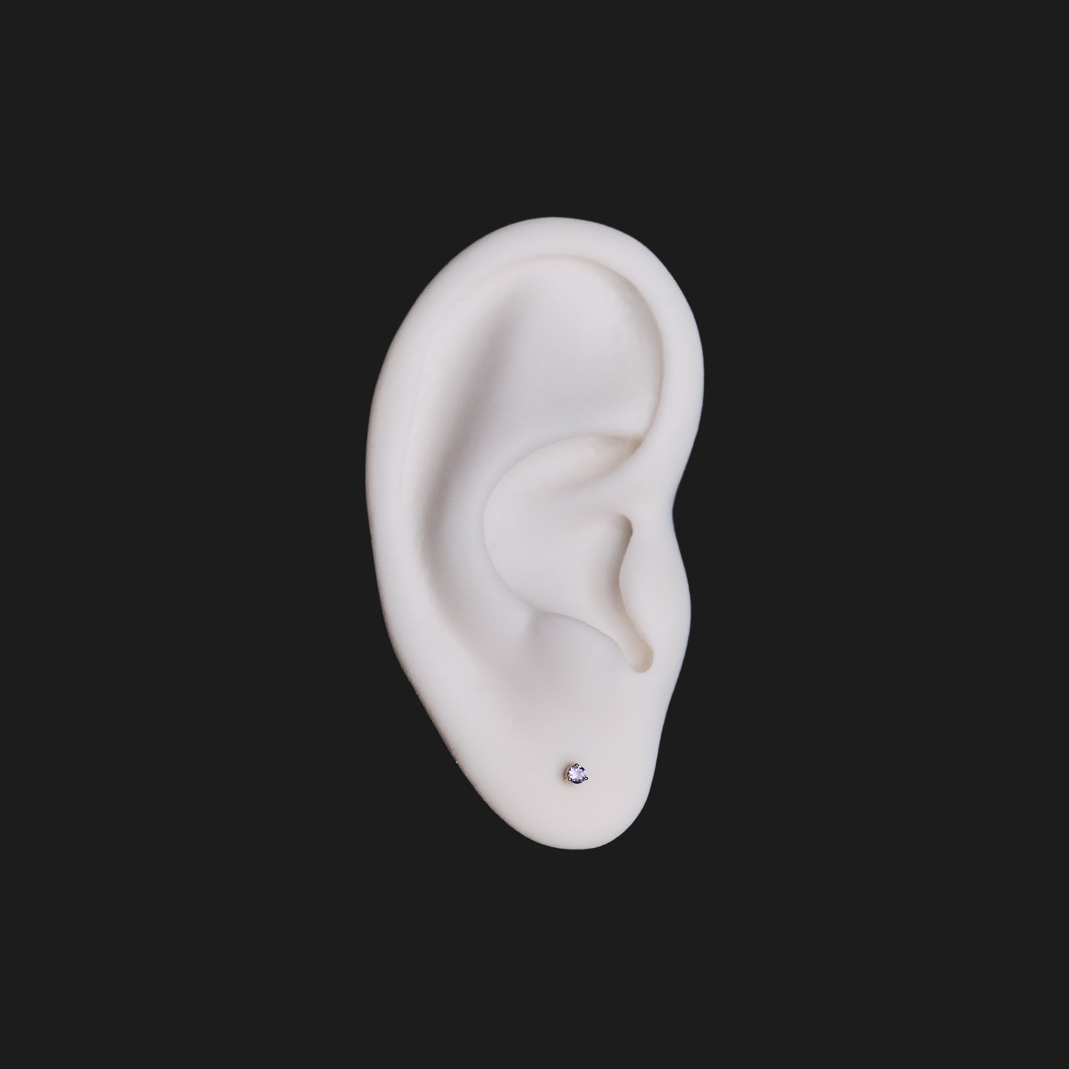 Fiat Lux 3 Prong Round Colored Gems (2mm) earring on white artificial ear, shown against a black background.