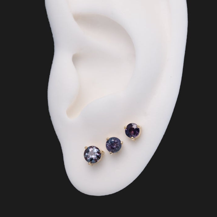 Three 3 Prong Round - Alexandrite (Limited Edition) labret studs in 14K gold worn on a white mannequin ear.
