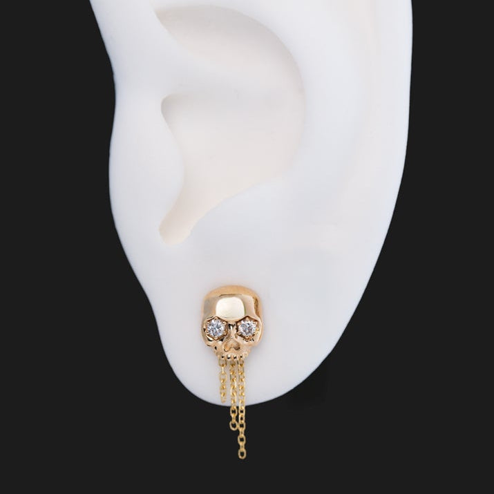 Fiat Lux The Skull Stud - Classic: 14k gold skull earring with diamond eyes and three short chain dangles on an ear model.