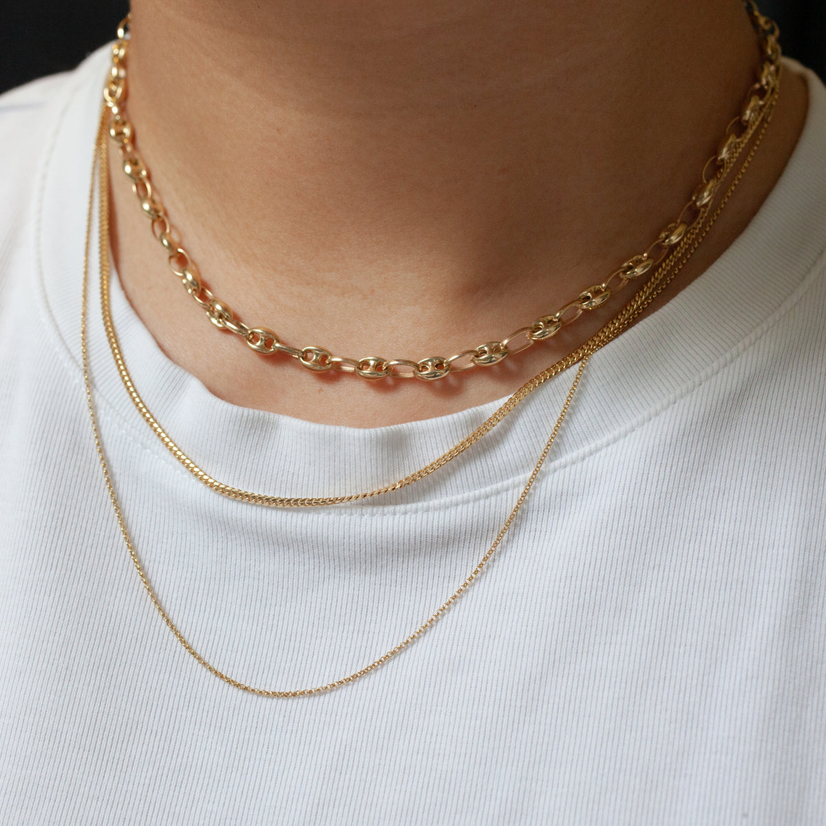 Fiat Lux’s Classic Cuban Chain (G) in 14K gold, layered on a white ribbed shirt for a bold statement look.