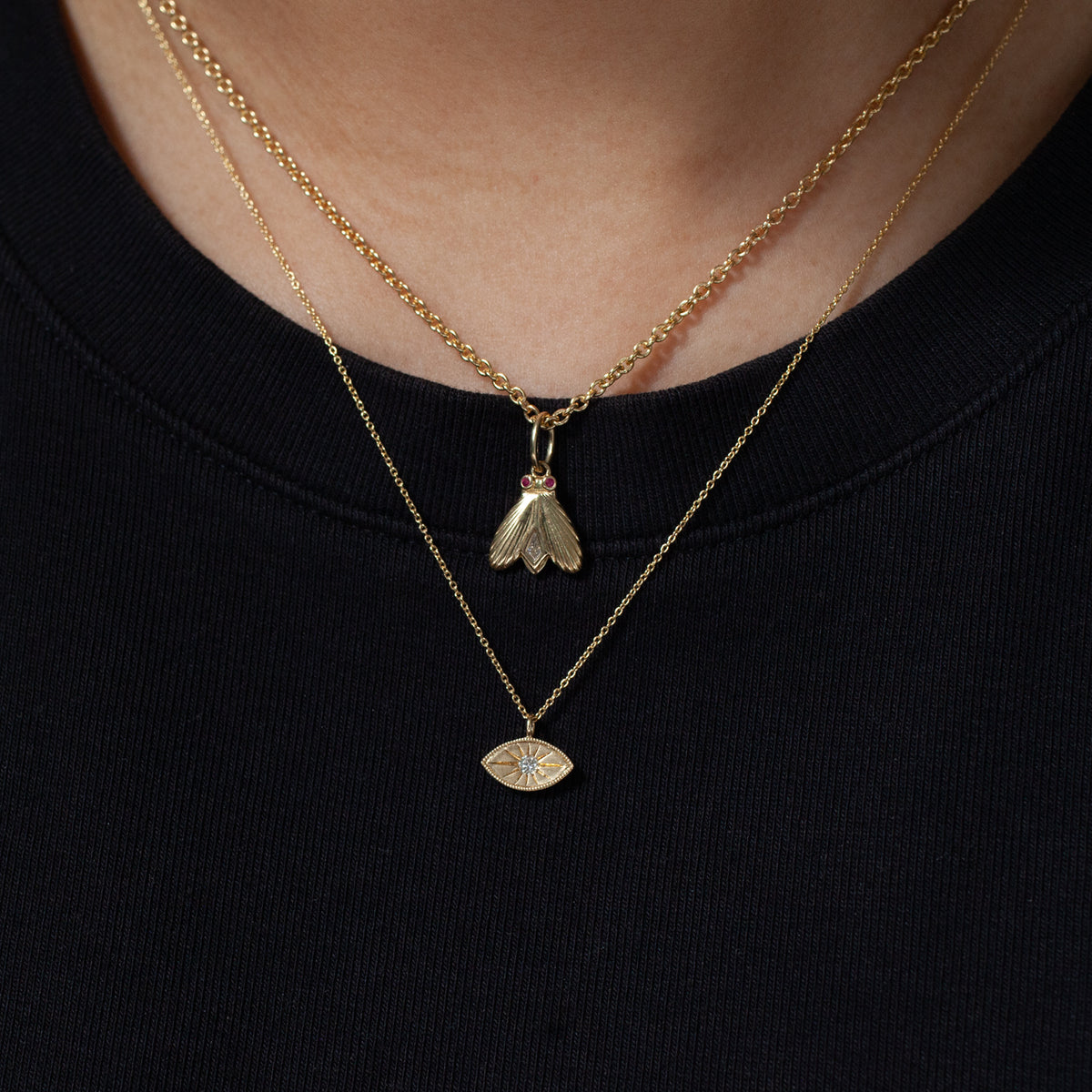 Two gold necklaces—a diamond charm and Fiat Lux Mini Mati—layered on black for a minimalist jewelry look.