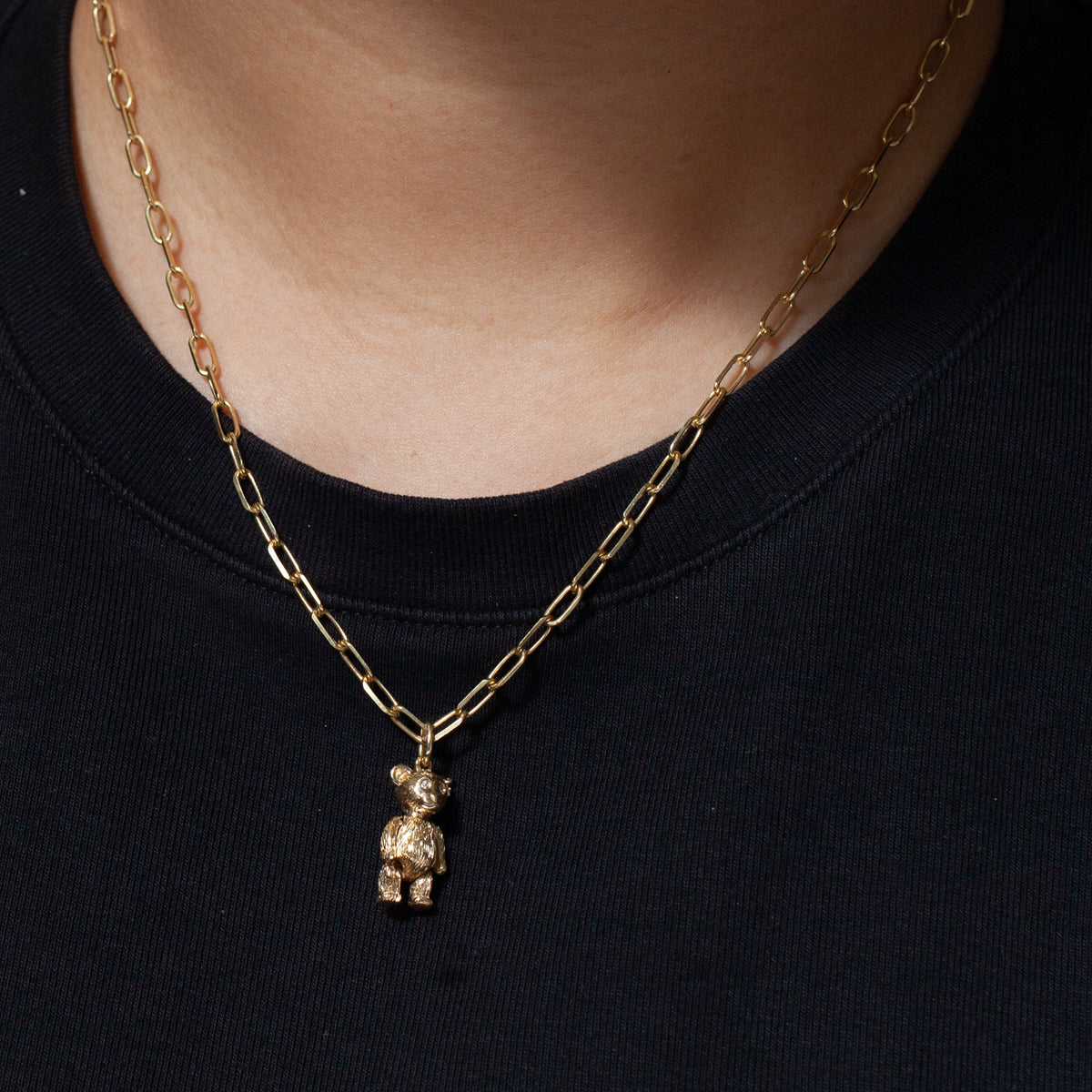 Fiat Lux Grande Paperclip Chain in 14K gold with teddy bear pendant, styled over a black shirt.
