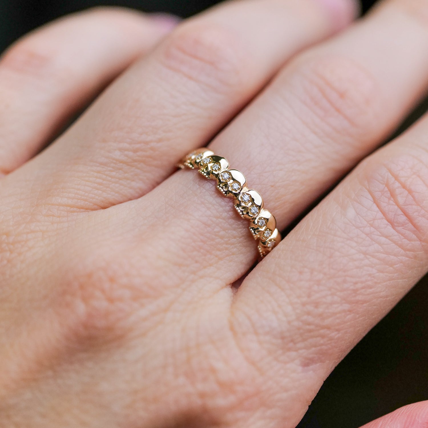 The Fiat Lux Eternity Skull Ring is worn, featuring 14k gold and seven small white diamonds.