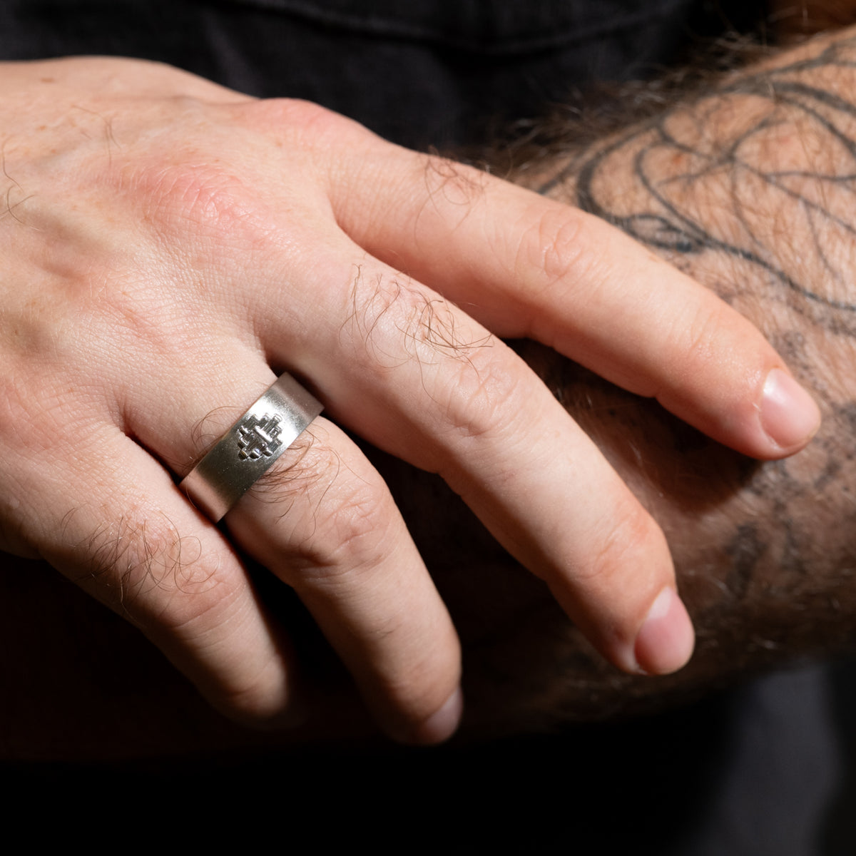 Wide Arcadia Ring featuring a silver band with an engraved cross and a diamond baguette band on a finger.