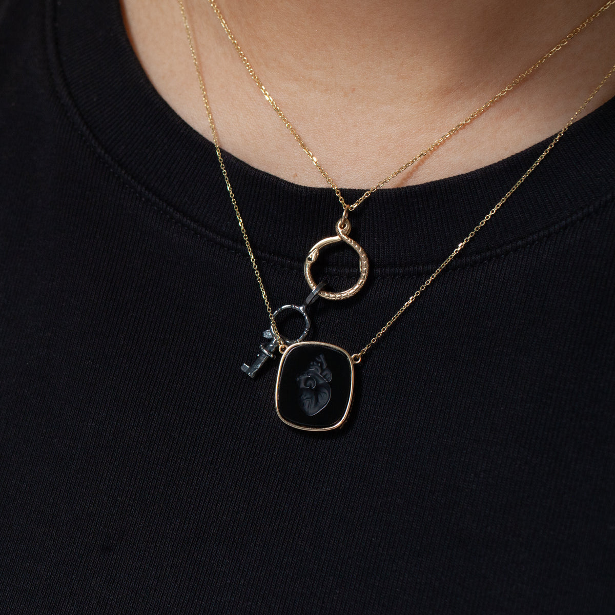 Two gold necklaces—a Heart Intaglio by Ioanna Eleftheriou—layered over a black shirt.