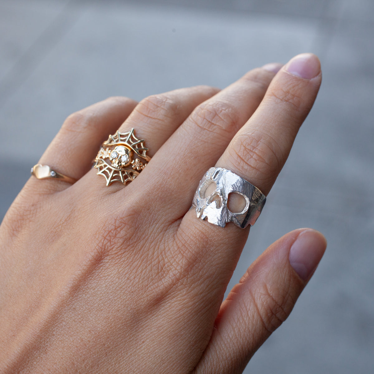 Three rings: a gold heart, gemmed spiderweb, and Ioanna Eleftheriou’s Nekrokefali Ring (S) on the middle finger.