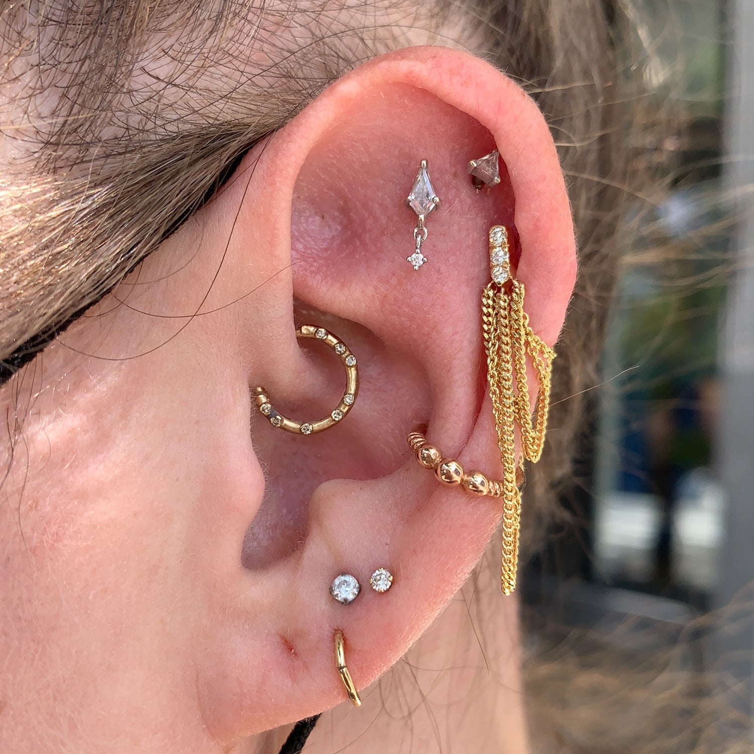 Close-up of an ear with Jack and G’s Chandelier Stud - Pavé in 14k gold and diamonds, plus hoops and a chain earring.