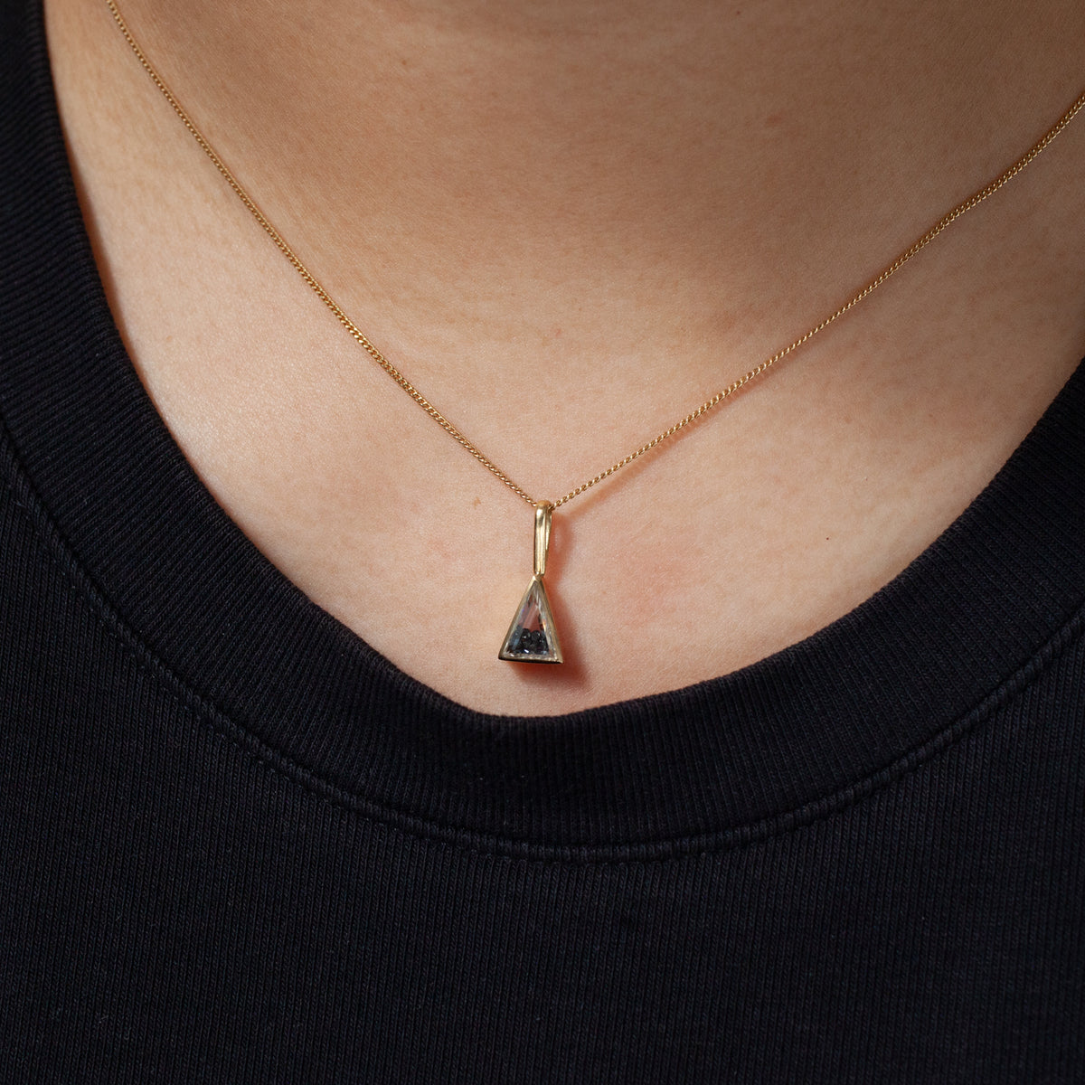 Moritz Glik’s Triangle Shaker Charm: gold chain, small triangular pendant with white sapphire, over a black top.