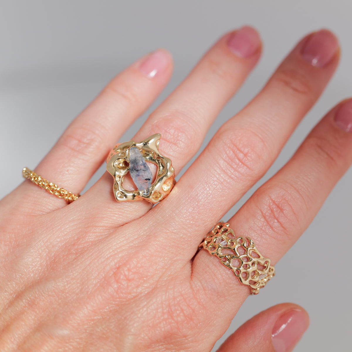 A hand with three gold rings, featuring the Nadia Faisal Yvonne Ring - Sapphire, set against a plain background.