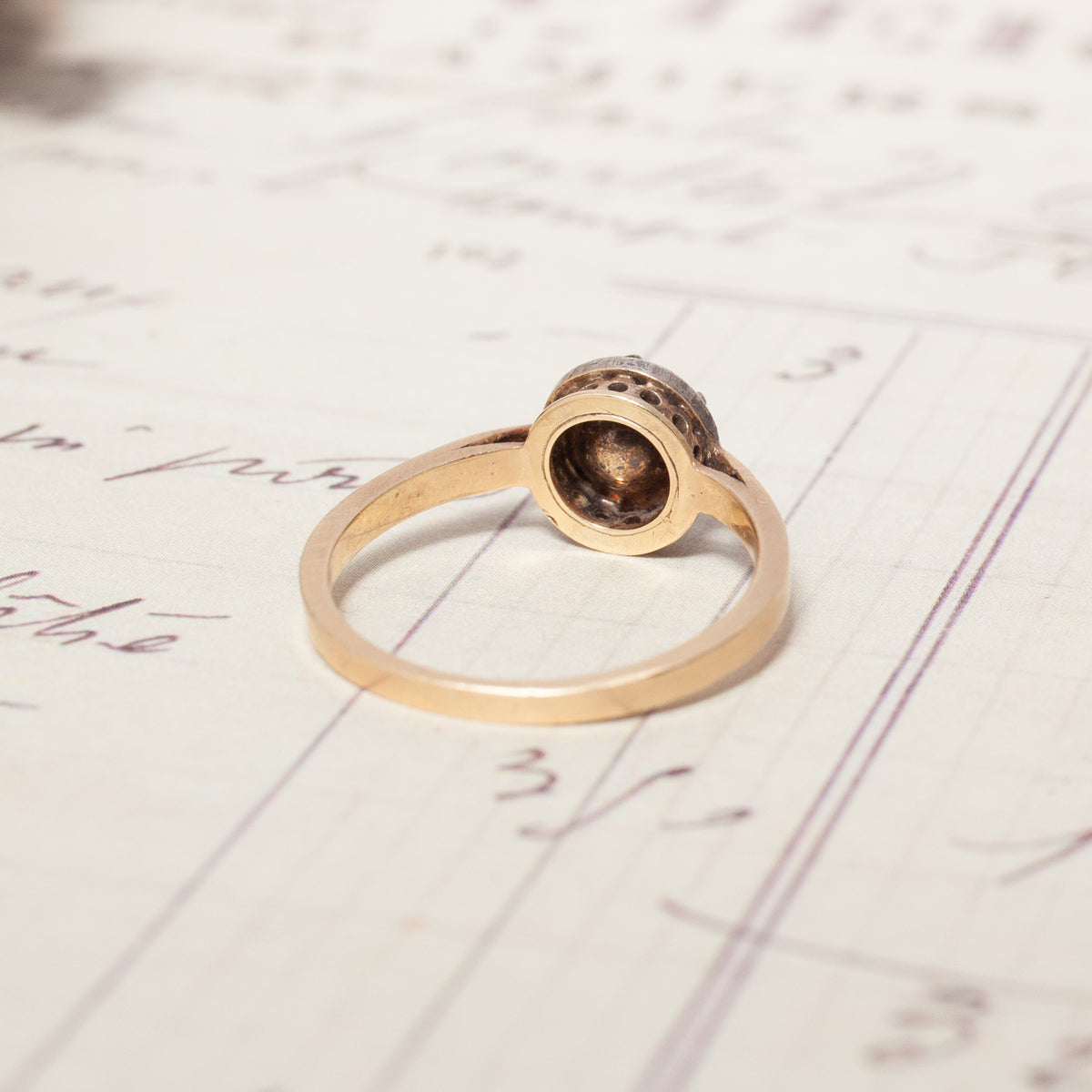 Antique Cut Down Collet Diamond Ring in gold resting on a vintage document.