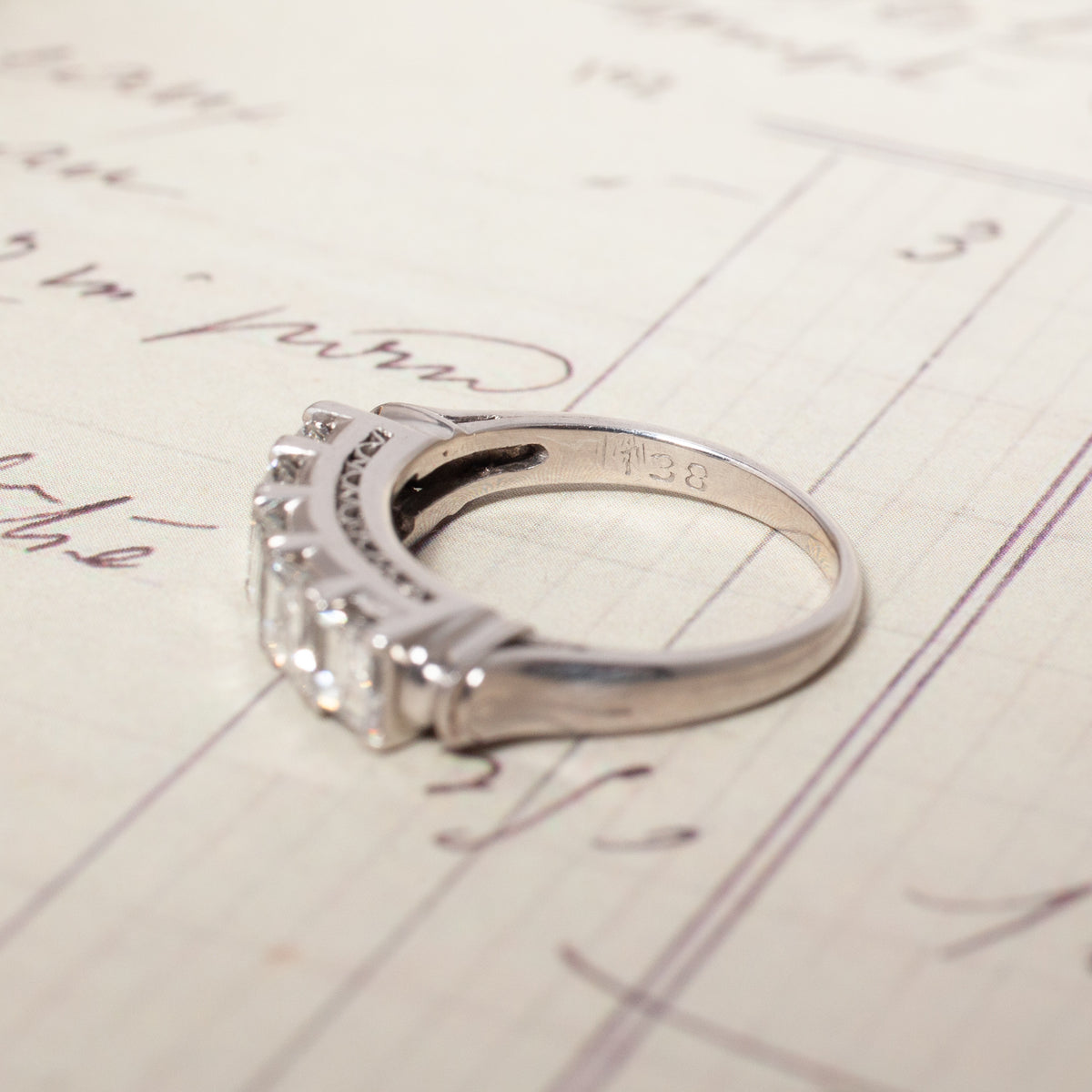 A Vintage Carré Cut Diamond Band - 4.5mm of platinum with four square-cut diamonds resting on a handwritten document.