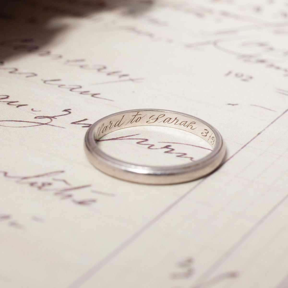 A Vintage Palladium Band inscribed Edward to Sarah 3.19 resting on a handwritten document.