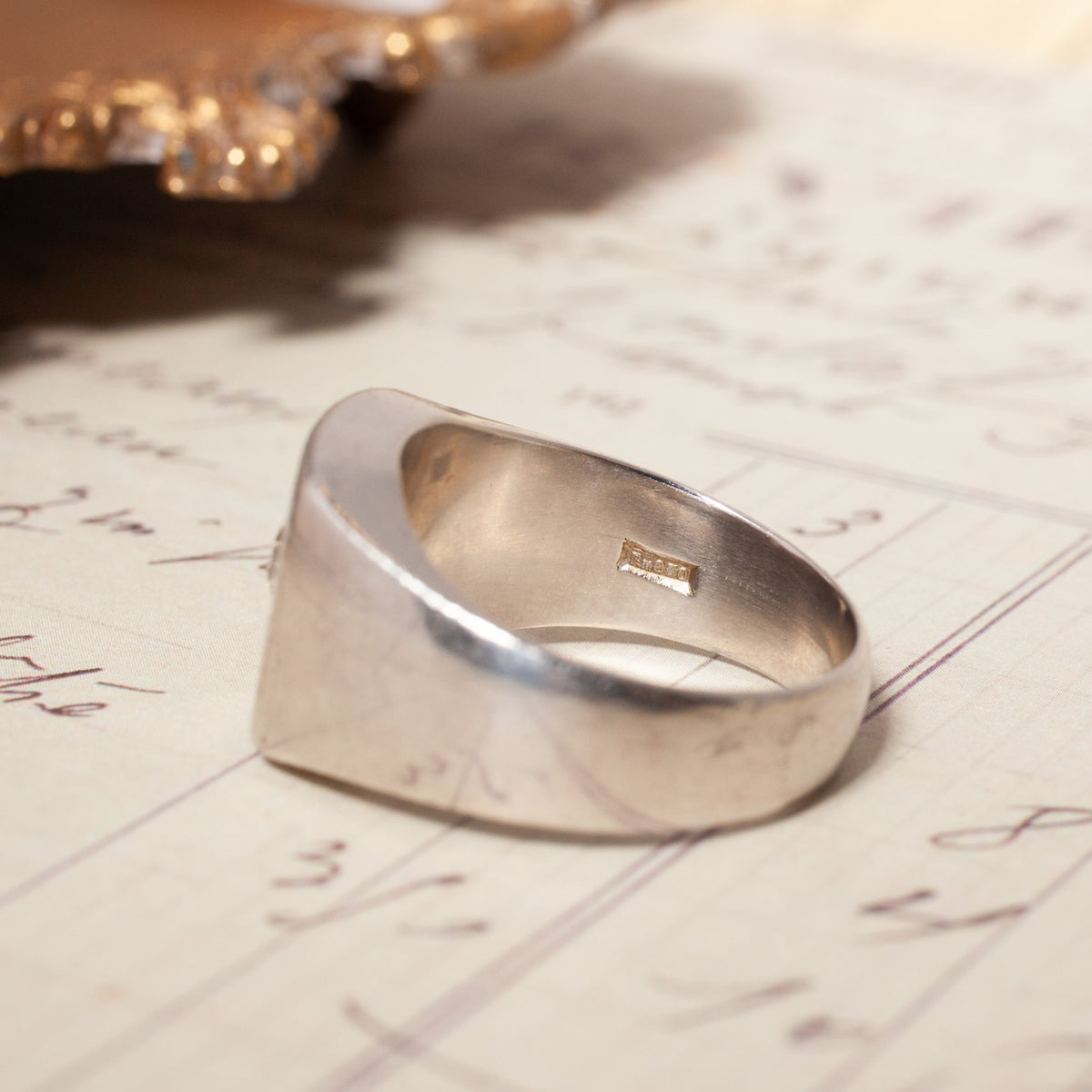 Vintage Star Set Square Signet platinum ring with an Old European Cut diamond resting on vintage script paper.