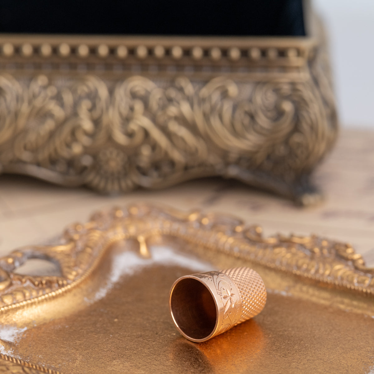 Gold-colored Vintage Engraved Thimble featuring an engraved plant motif, resting on a small decorative tray.