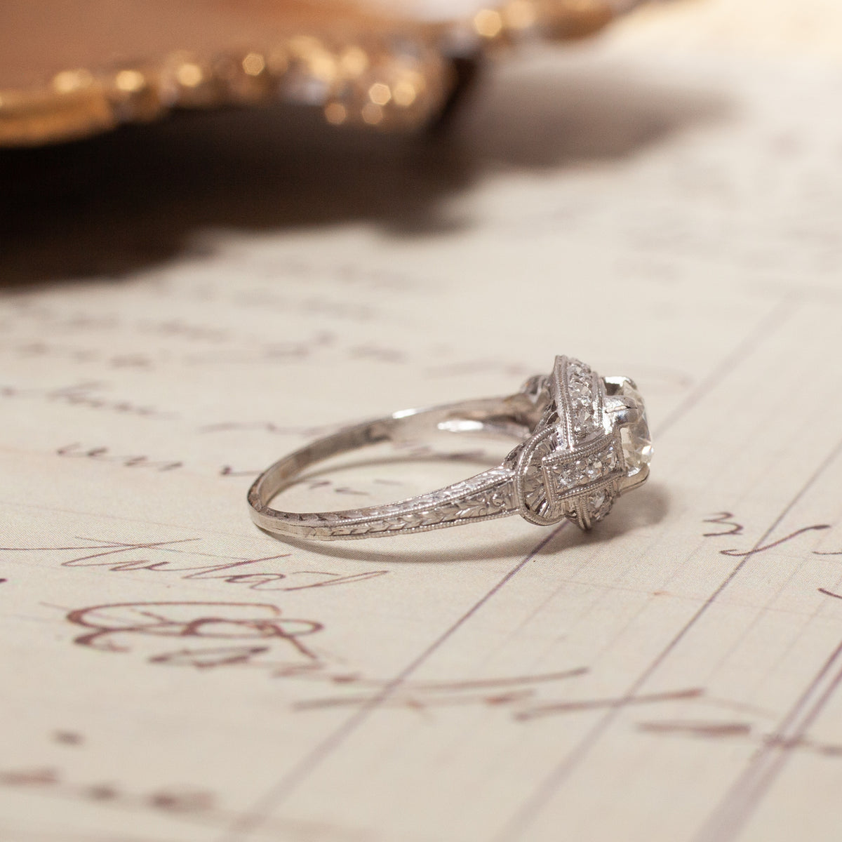 An intricate 18K white gold Vintage Transitional Cut Diamond Halo Ring resting on a handwritten document.