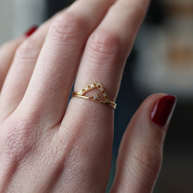 A hand with red nails wears DMD Metal’s Cassat Ring, a 14K gold geometric band with small white diamonds.